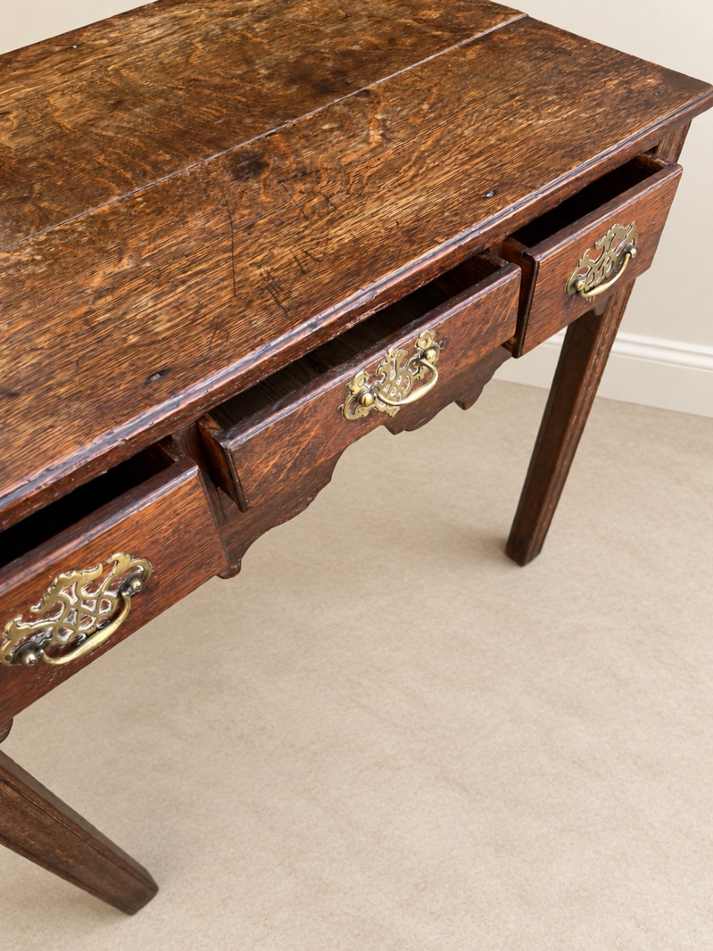 An 18th-century dark oak lowboy side table featuring three drawers with brass handles and a scalloped apron. View VIII