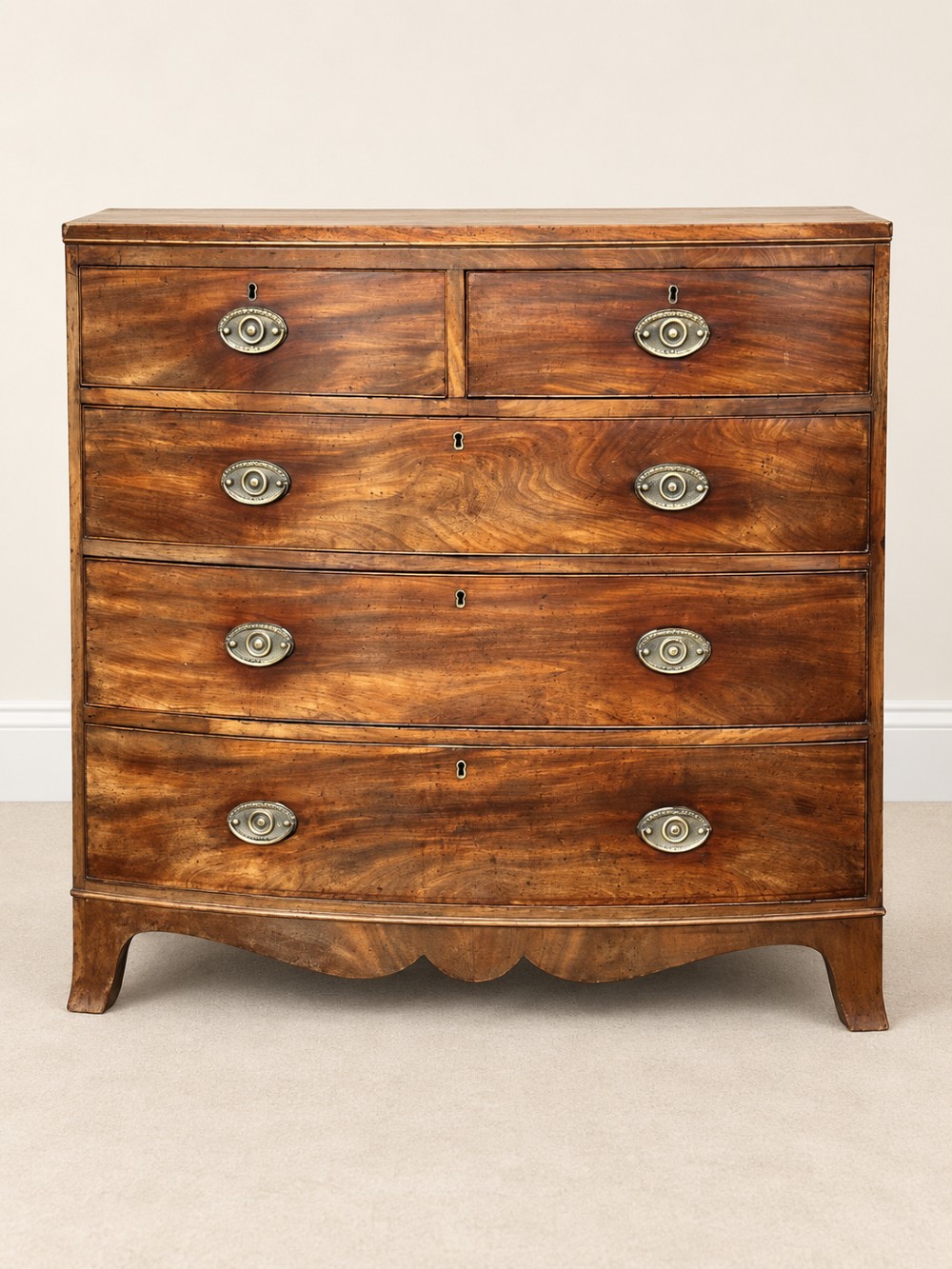 A nineteenth-century mahogany bowfront chest featuring two short over three long graduated drawers with oval brass handles.