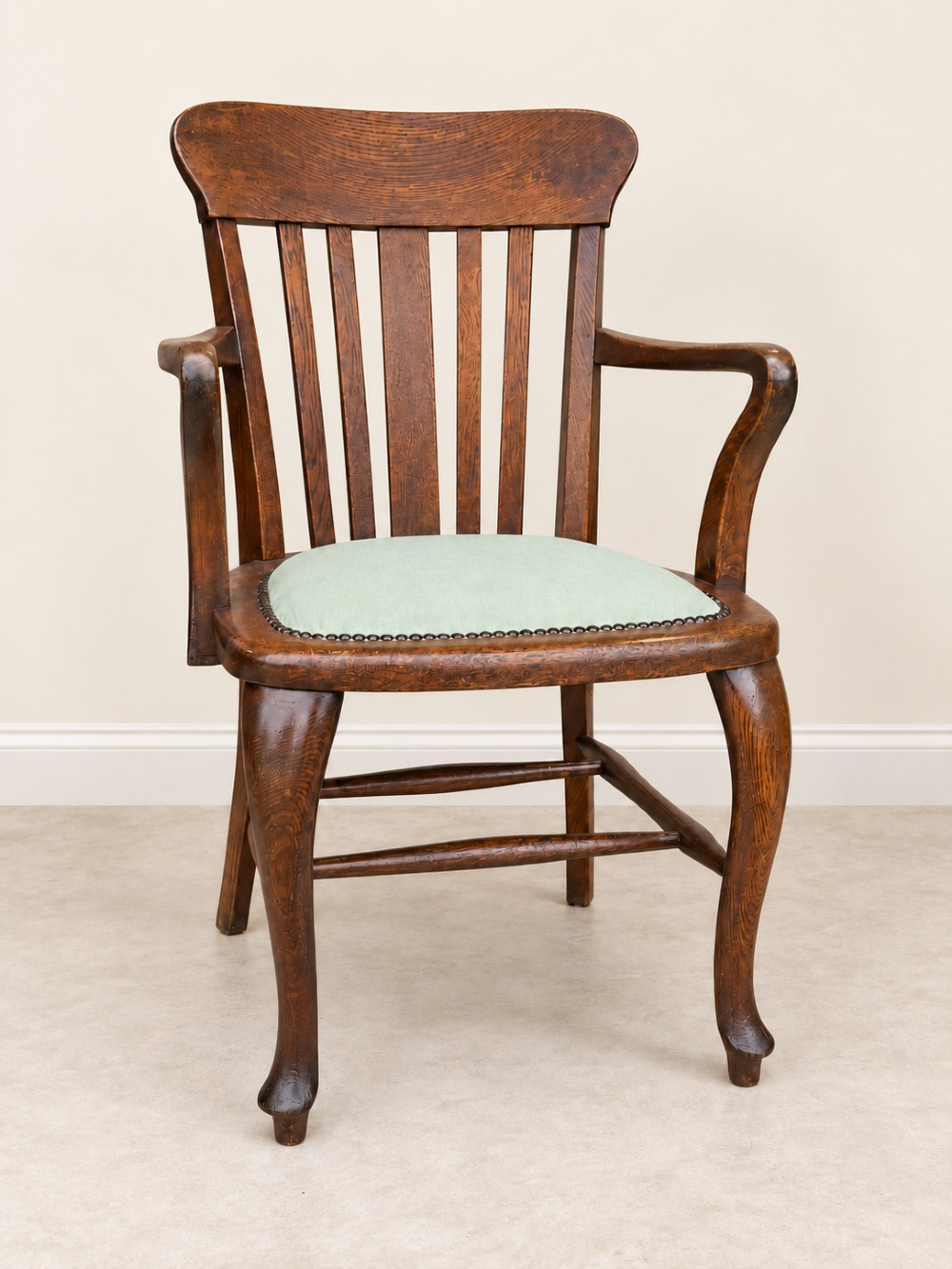 A late 19th-century oak office chair featuring a slatted backrest, curved armrests, cabriole front legs, and a pale green fabric seat secured with metal studs.
