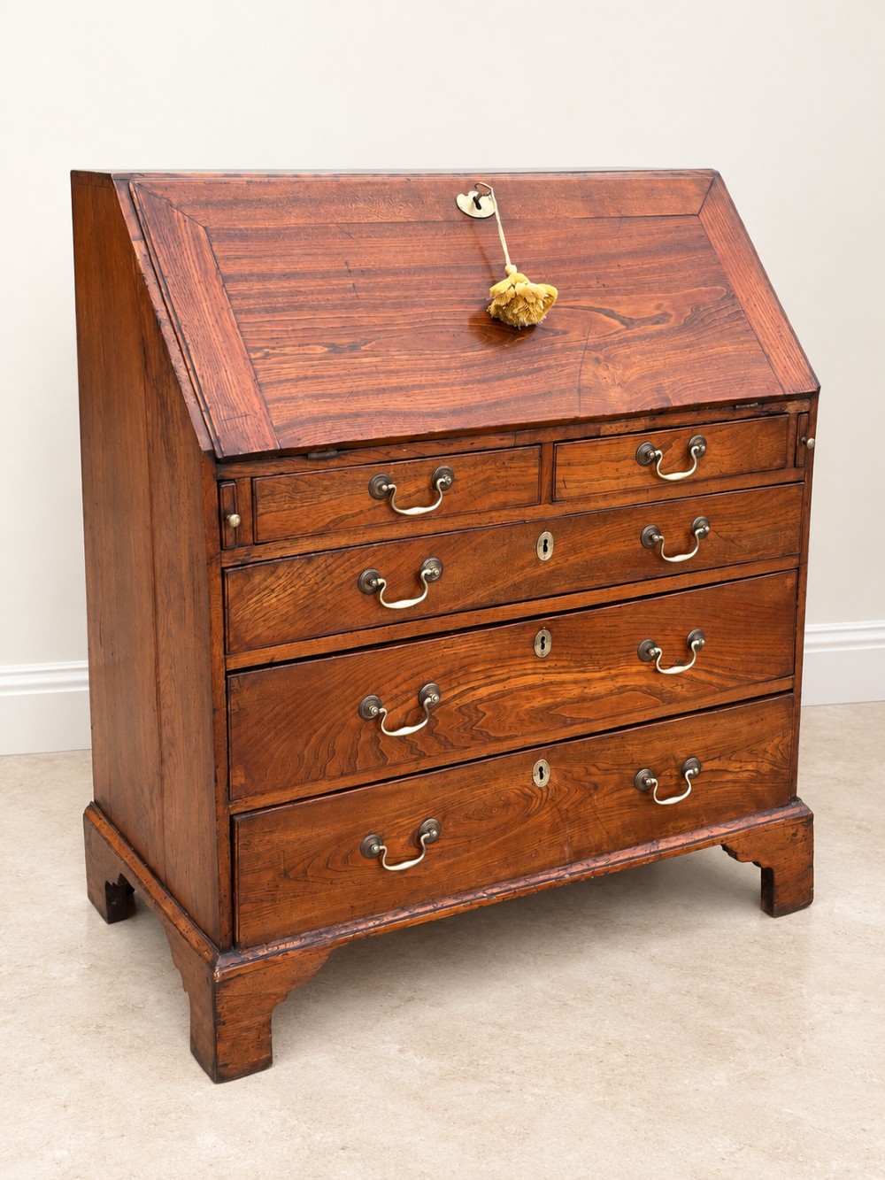 An antique Georgian warm brown elm slant-front writing bureau with four drawers, brass handles, and bracket feet. View II