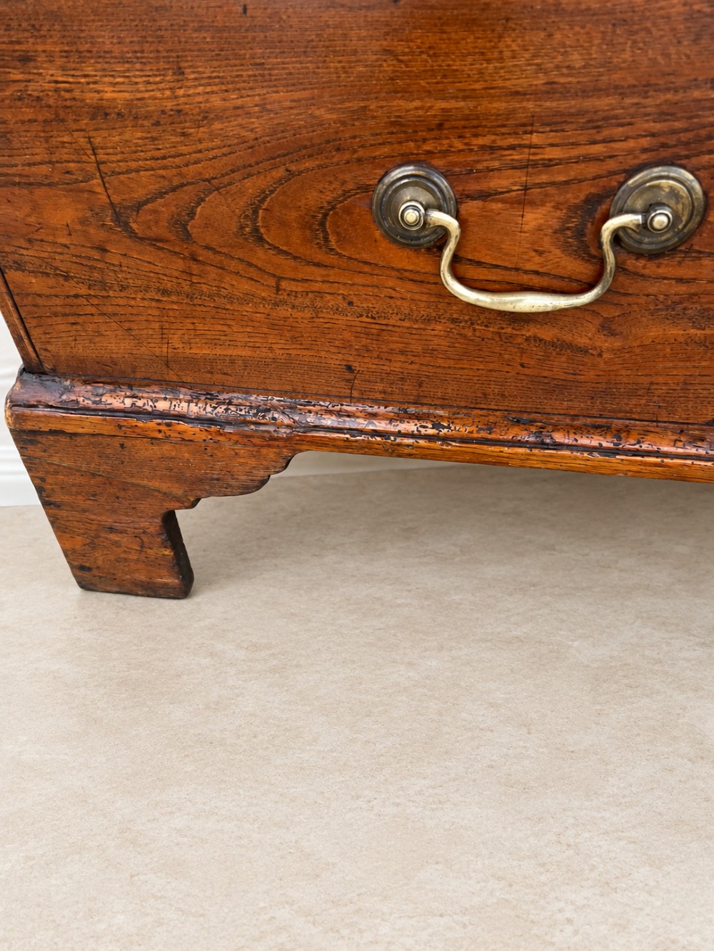 An antique Georgian warm brown elm slant-front writing bureau with four drawers, brass handles, and bracket feet. View V