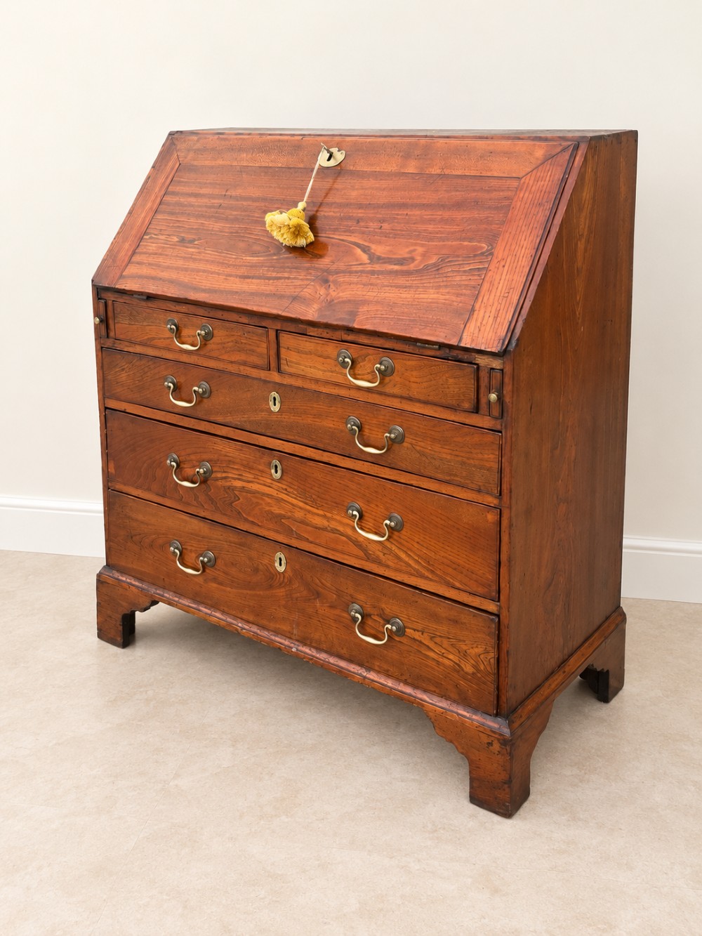 An antique Georgian warm brown elm slant-front writing bureau with four drawers, brass handles, and bracket feet. View VI