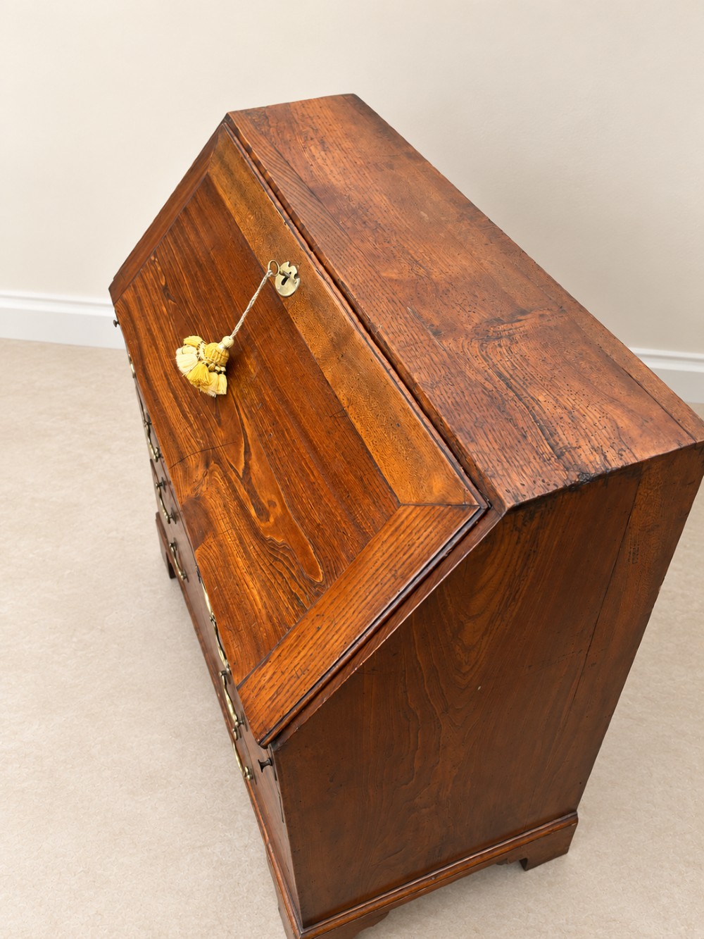 An antique Georgian warm brown elm slant-front writing bureau with four drawers, brass handles, and bracket feet. View VII