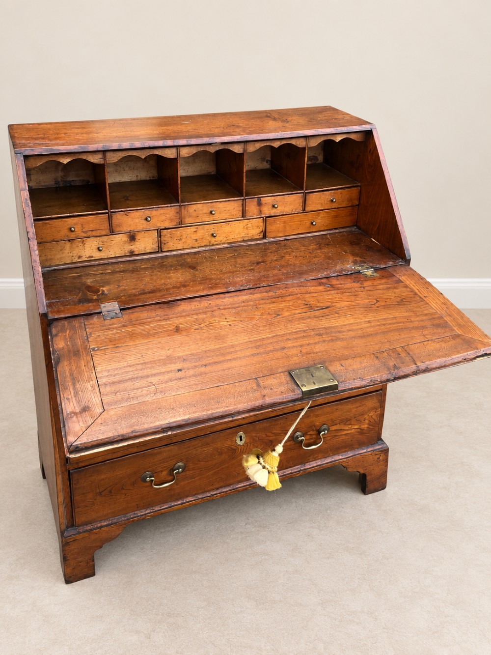 An antique Georgian warm brown elm slant-front writing bureau with four drawers, brass handles, and bracket feet. View IX