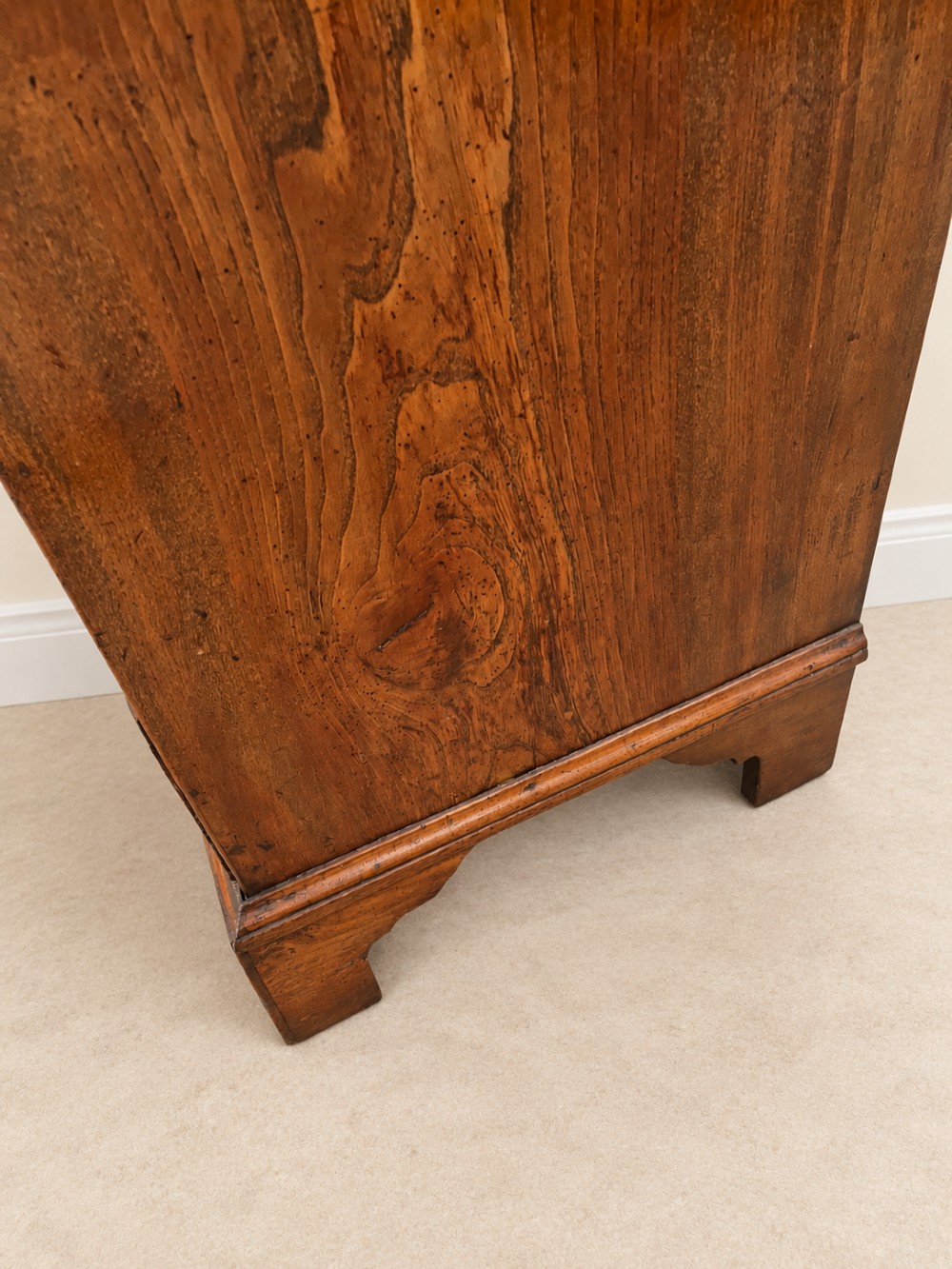 An antique Georgian warm brown elm slant-front writing bureau with four drawers, brass handles, and bracket feet. View XI