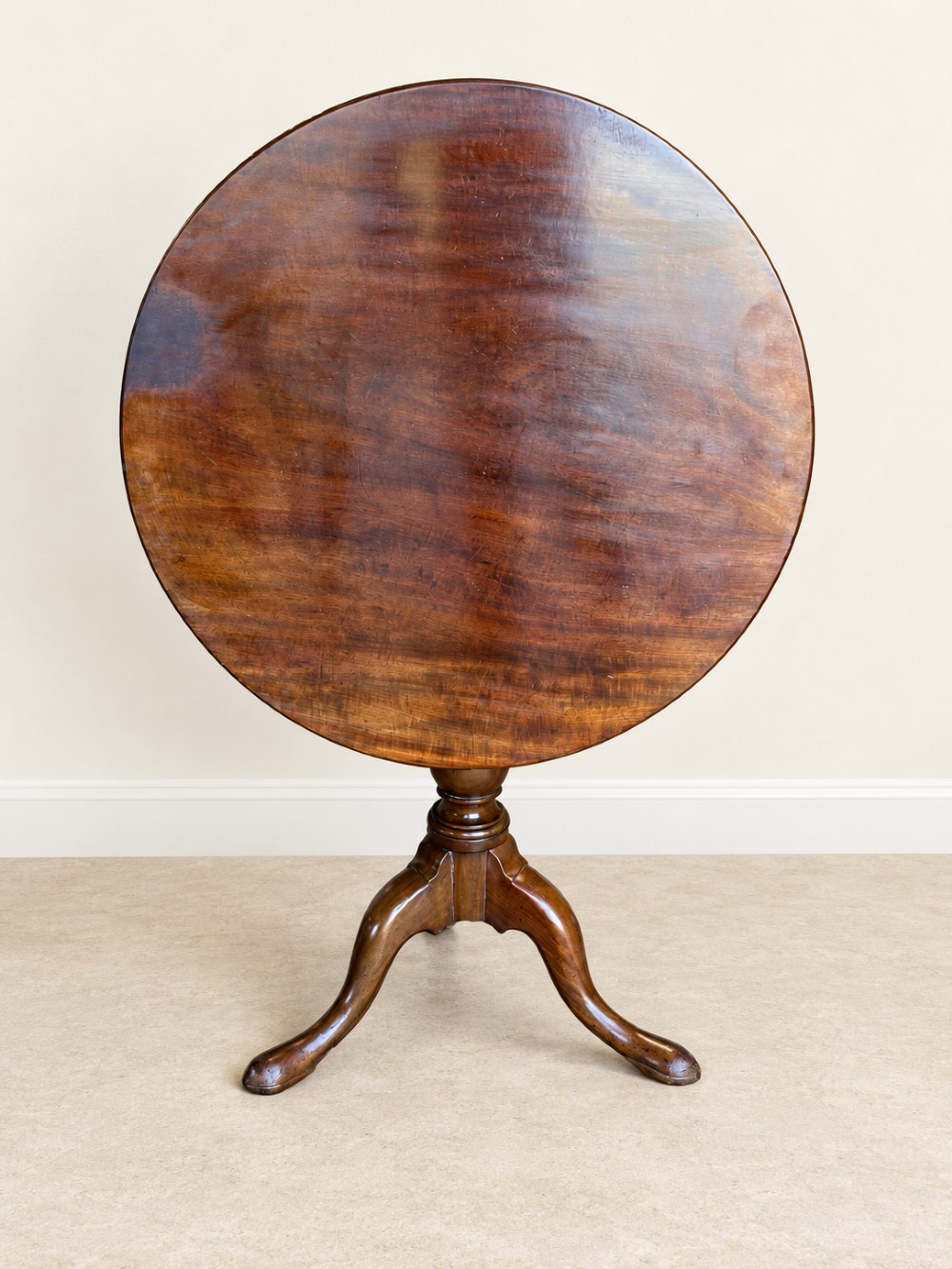 An 18th-century Georgian mahogany tilt-top table shown with its circular top locked vertically above a turned pedestal base with three cabriole legs. View II