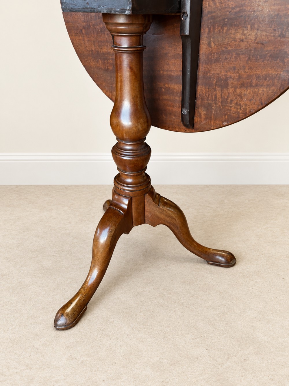 An 18th-century Georgian mahogany tilt-top table shown with its circular top locked vertically above a turned pedestal base with three cabriole legs. View III
