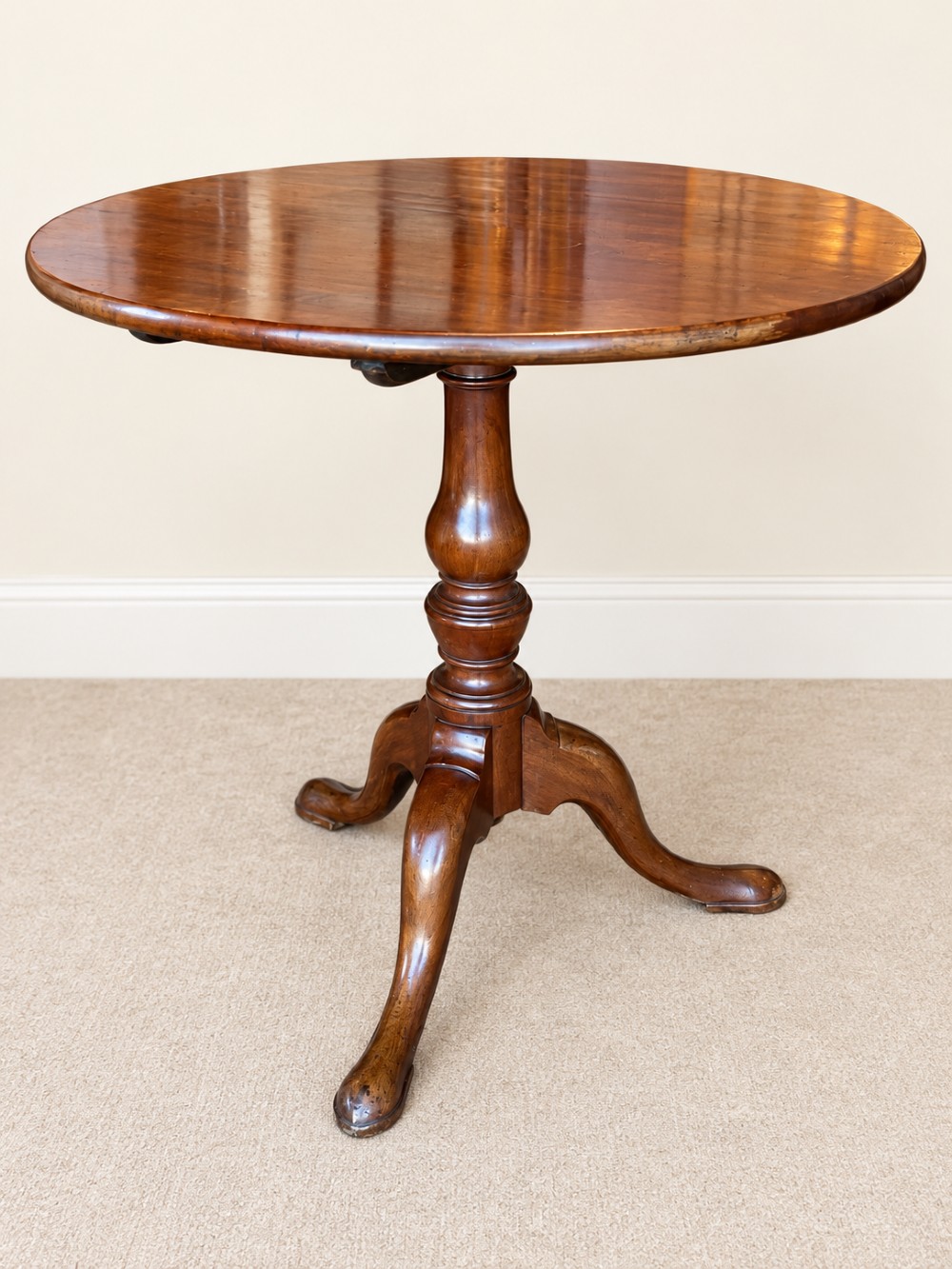 An 18th-century Georgian mahogany tilt-top table shown with its circular top locked vertically above a turned pedestal base with three cabriole legs. View V