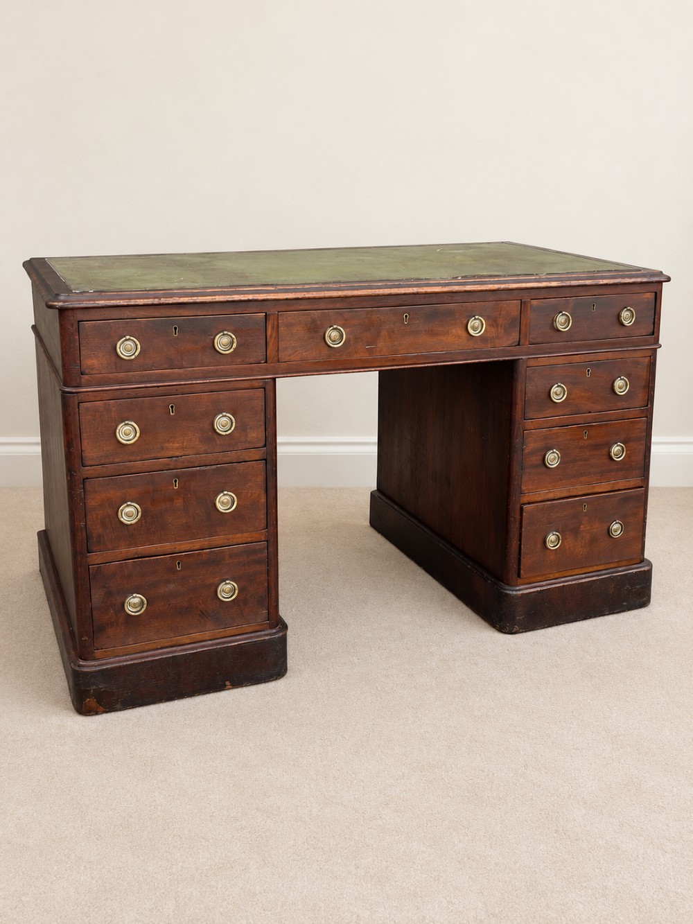 A 19th-century dark mahogany pedestal desk featuring nine drawers with brass handles and an inset green leather writing surface.
