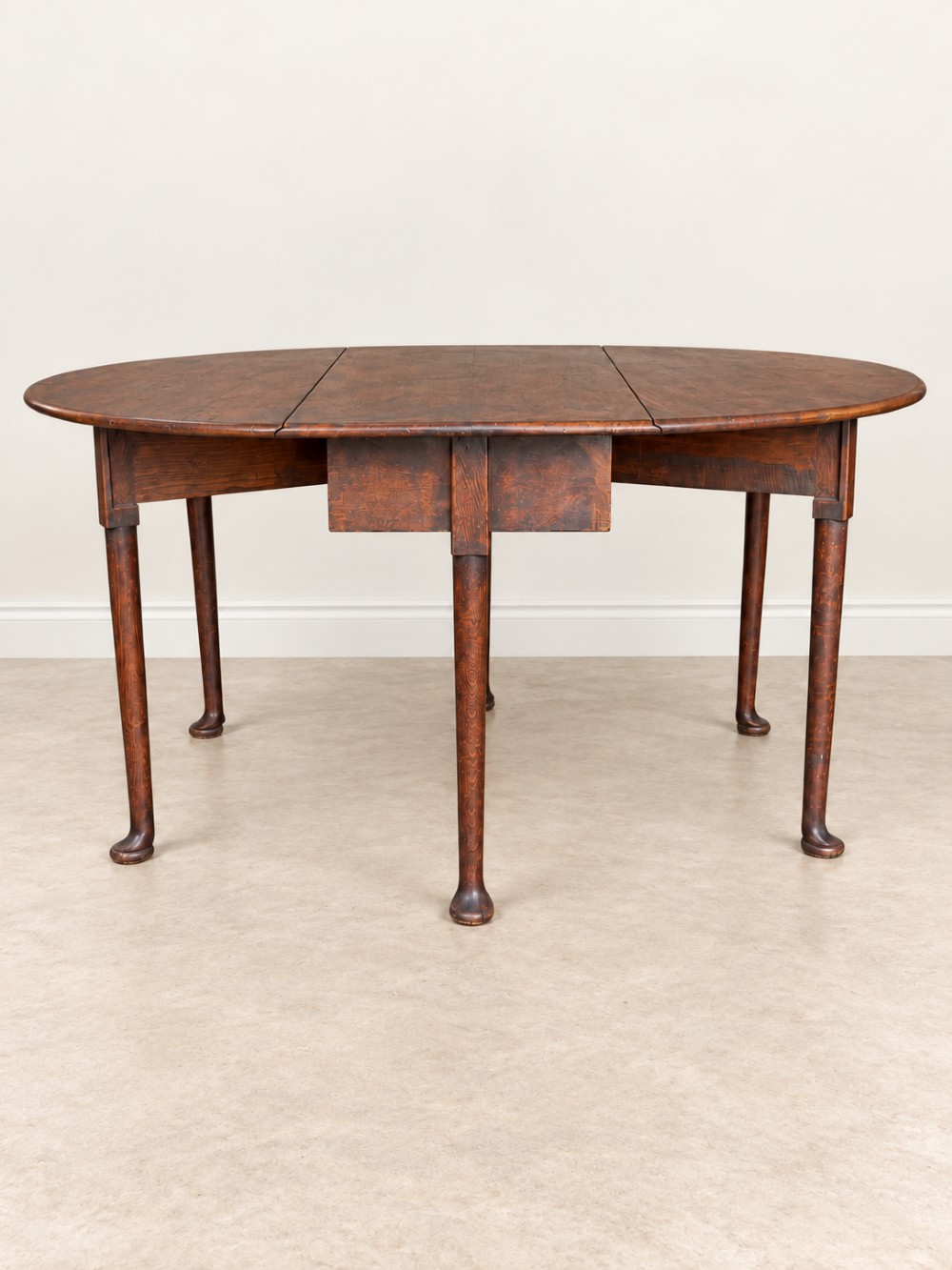 An antique Georgian dark oak drop-leaf dining table featuring an oval tabletop supported by gatelegs and pad feet.