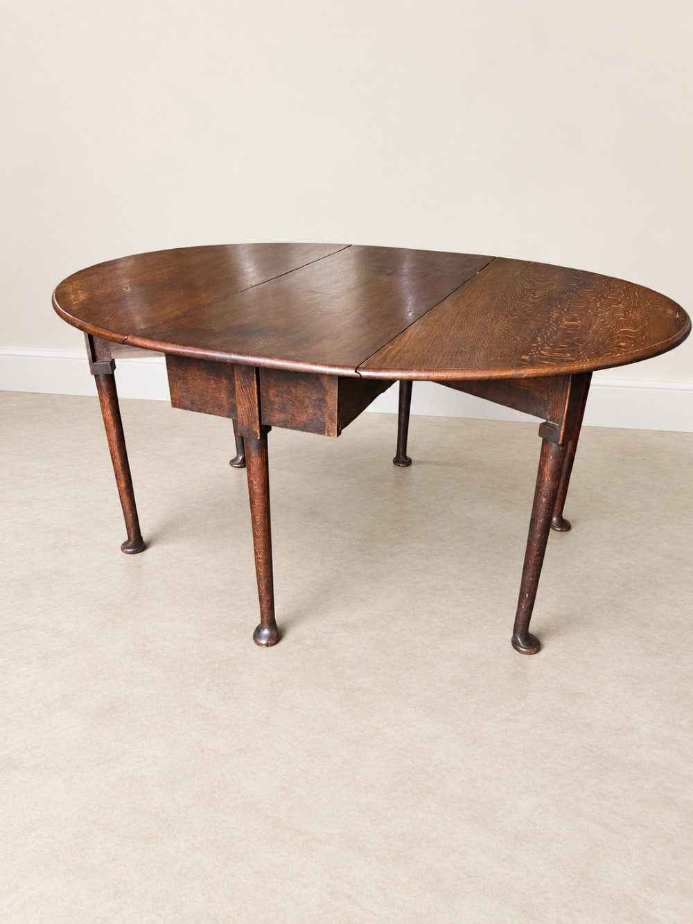 An antique Georgian dark oak drop-leaf dining table featuring an oval tabletop supported by gatelegs and pad feet. View II
