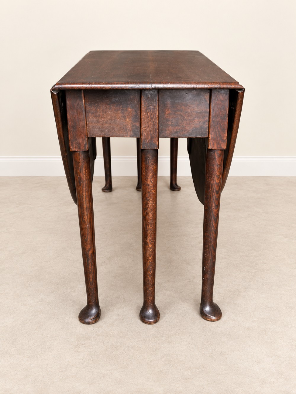 An antique Georgian dark oak drop-leaf dining table featuring an oval tabletop supported by gatelegs and pad feet. View IV