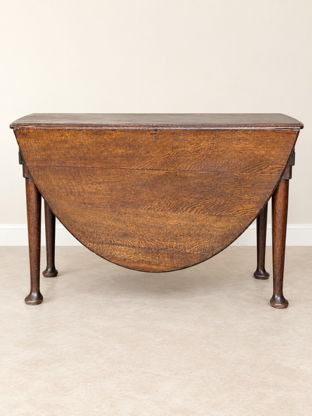 An antique Georgian dark oak drop-leaf dining table featuring an oval tabletop supported by gatelegs and pad feet. View V