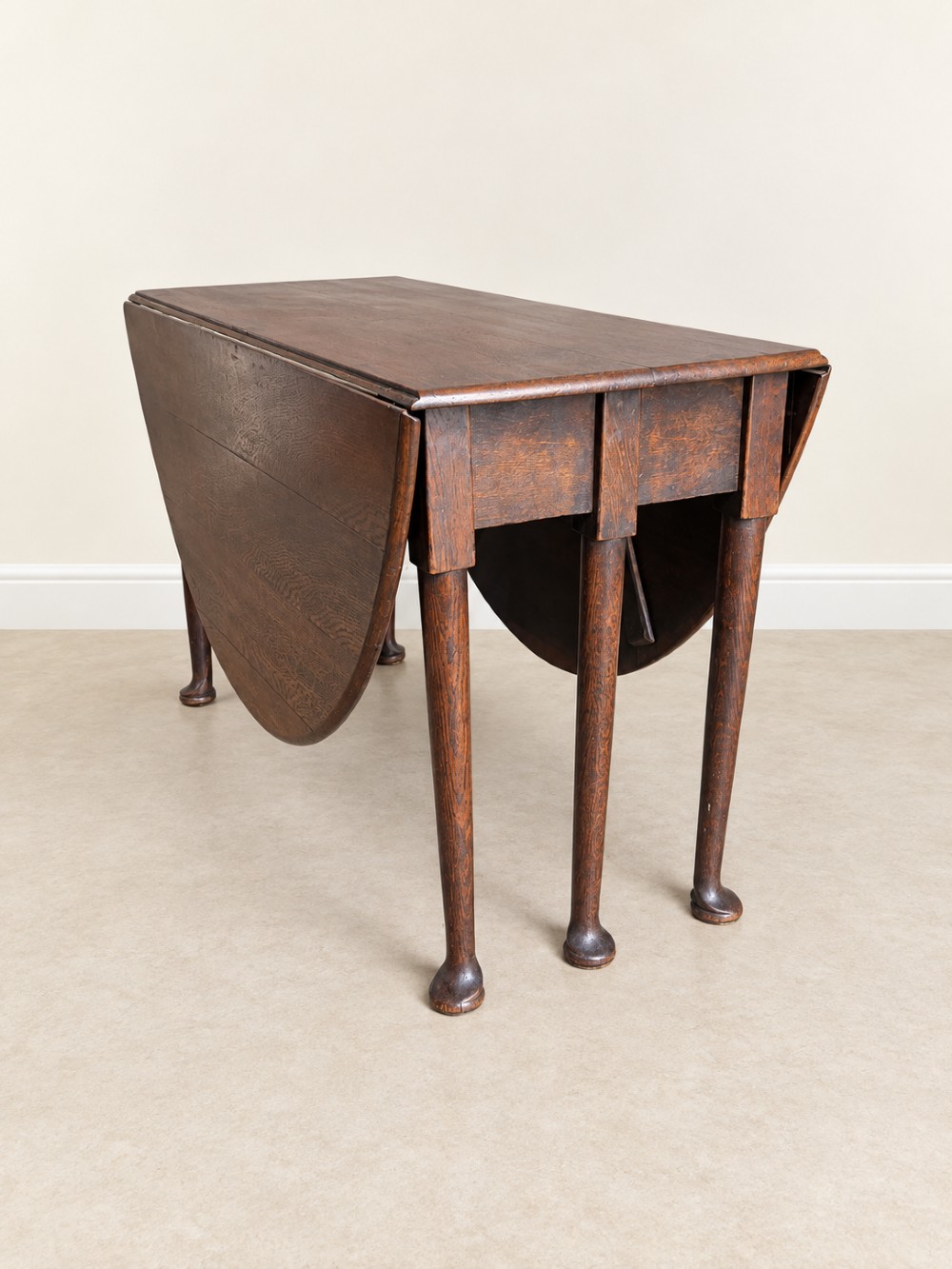 An antique Georgian dark oak drop-leaf dining table featuring an oval tabletop supported by gatelegs and pad feet. View VI