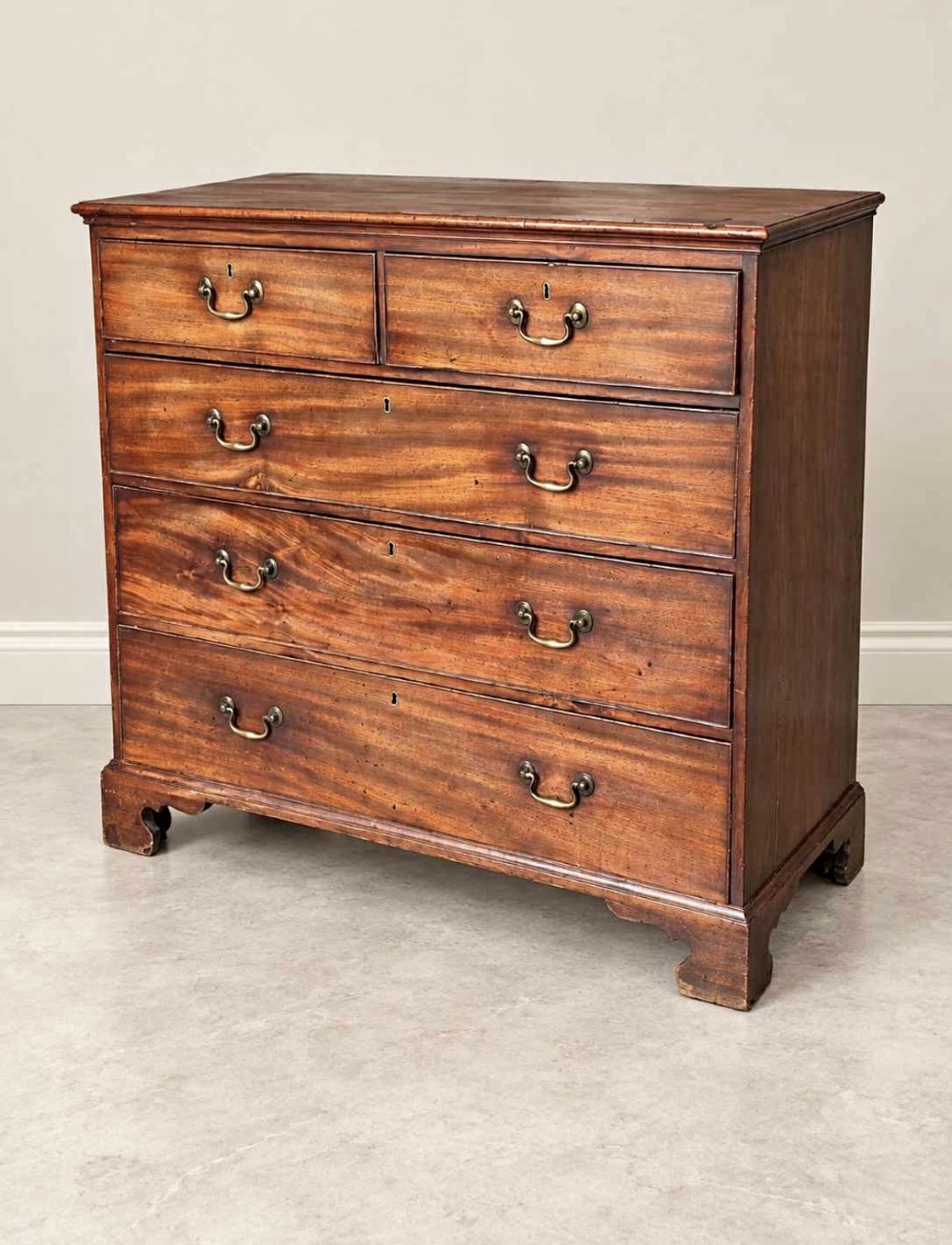An antique Georgian mahogany chest of drawers featuring a two-over-three drawer configuration, brass swan-neck handles, escutcheons, and bracket feet.