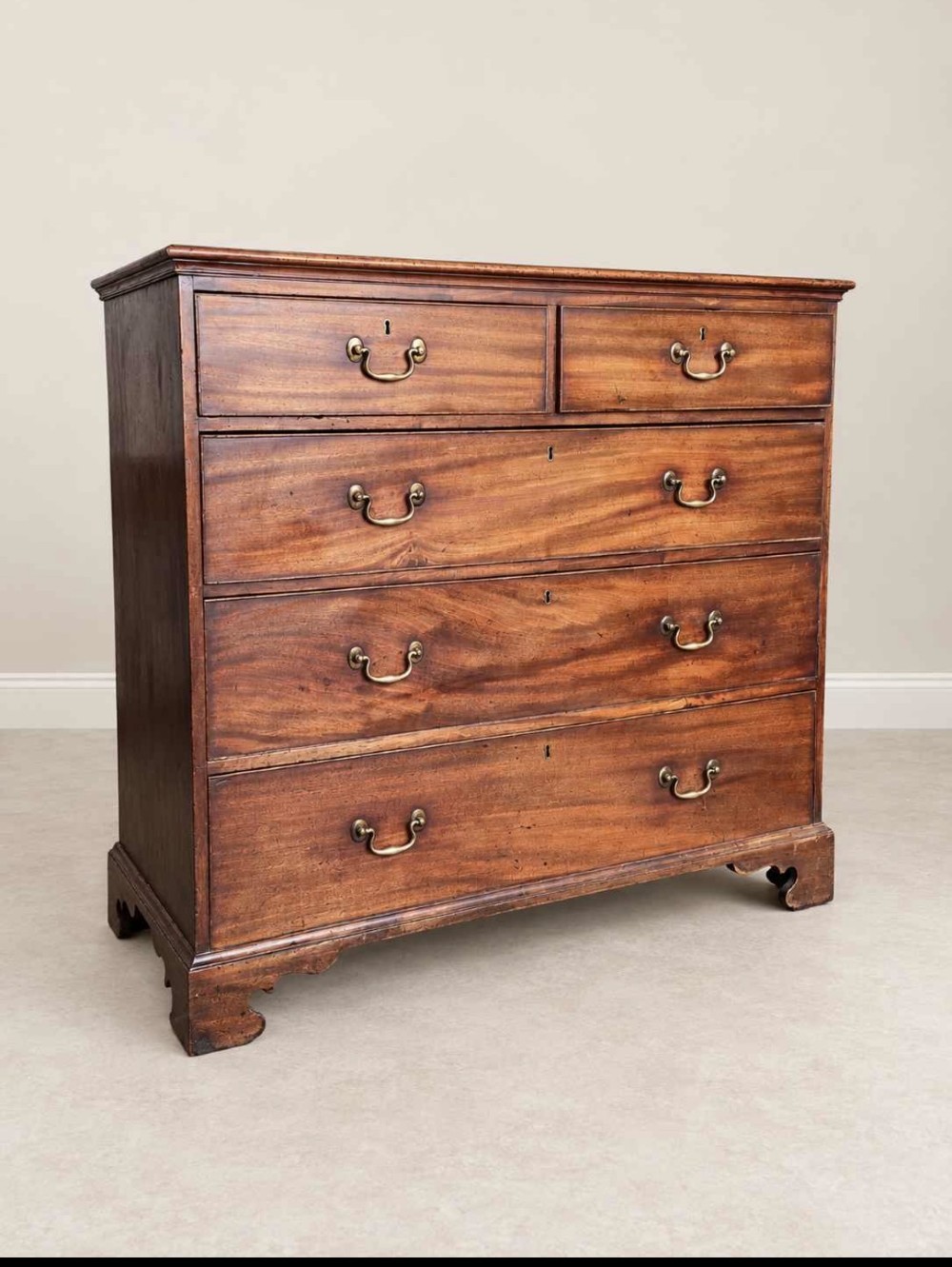 An antique Georgian mahogany chest of drawers featuring a two-over-three drawer configuration, brass swan-neck handles, escutcheons, and bracket feet. View II