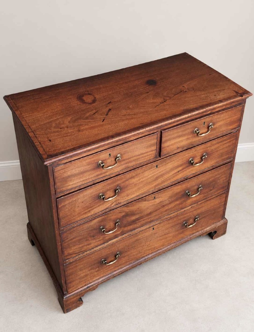 An antique Georgian mahogany chest of drawers featuring a two-over-three drawer configuration, brass swan-neck handles, escutcheons, and bracket feet. View III