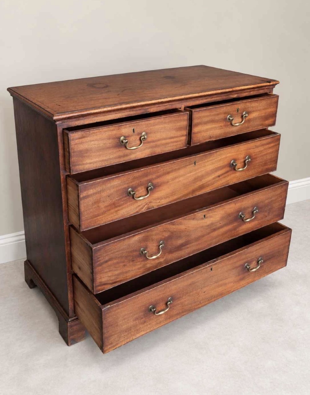 An antique Georgian mahogany chest of drawers featuring a two-over-three drawer configuration, brass swan-neck handles, escutcheons, and bracket feet. View V