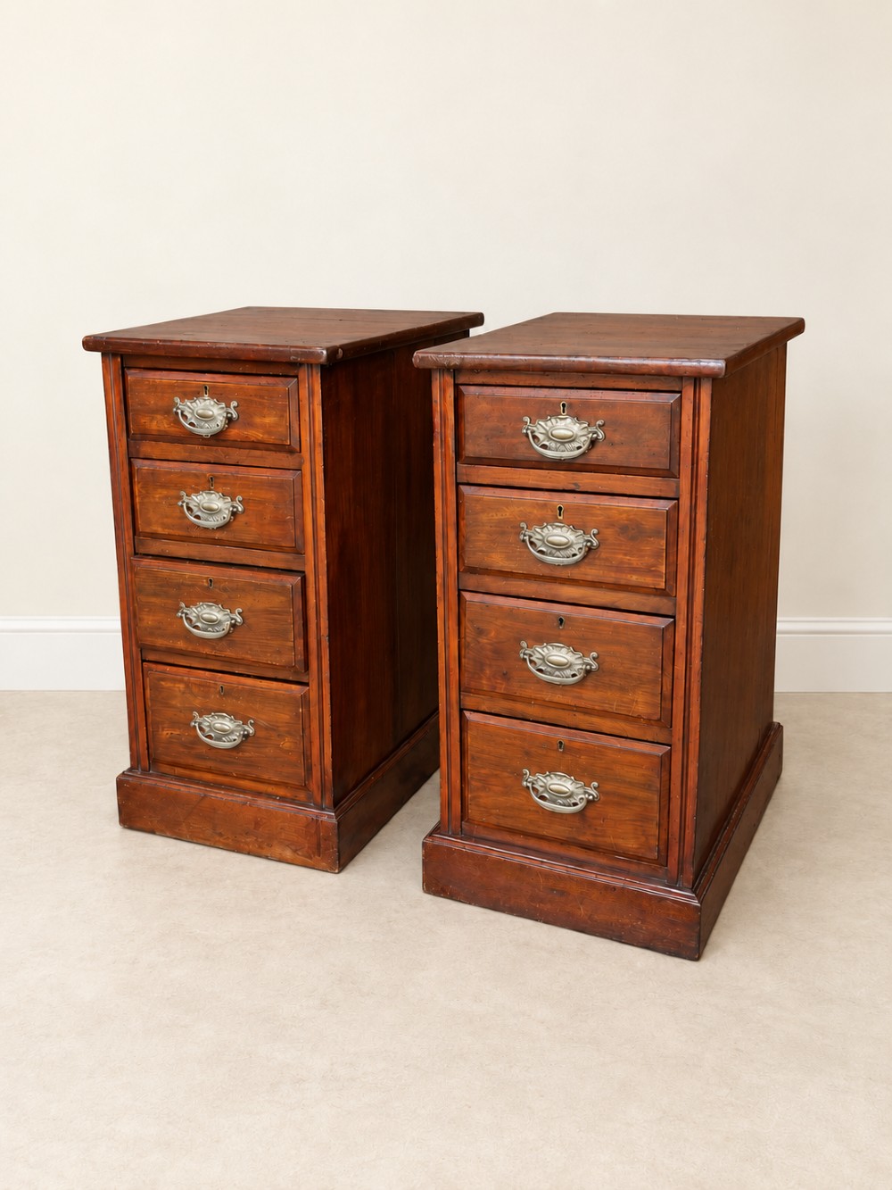 A pair of late Victorian mahogany bedside chests, each featuring four drawers with metal swing handles and a solid plinth base.