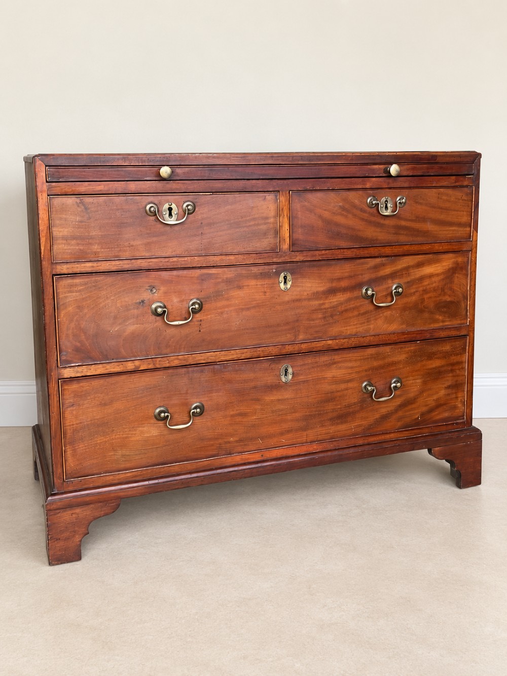 A Georgian mahogany bachelors chest featuring a brushing slide, two short over two long drawers, brass swan-neck handles, and bracket feet.