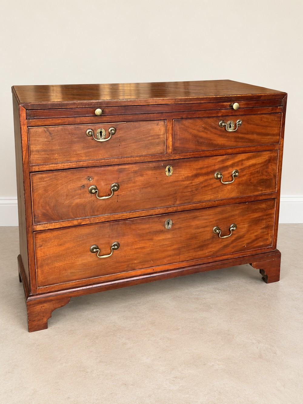 A Georgian mahogany bachelors chest featuring a brushing slide, two short over two long drawers, brass swan-neck handles, and bracket feet. View II