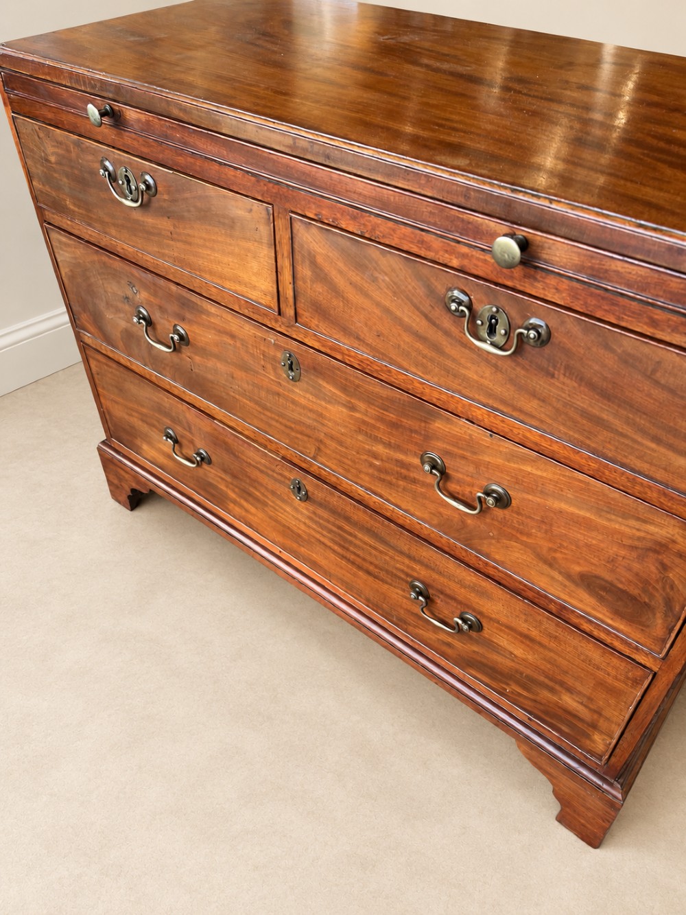 A Georgian mahogany bachelors chest featuring a brushing slide, two short over two long drawers, brass swan-neck handles, and bracket feet. View V