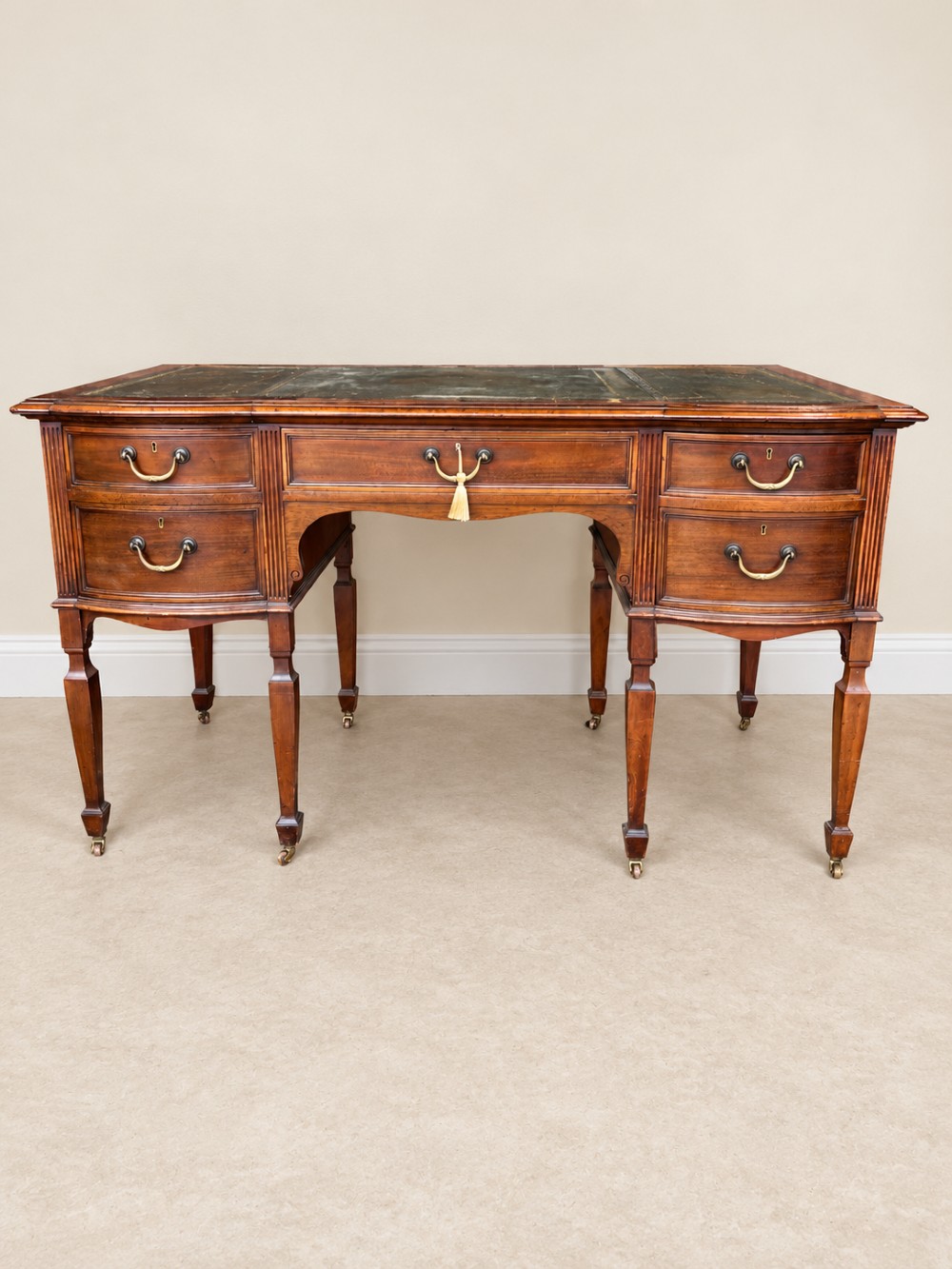 Late nineteenth-century mahogany writing desk featuring an inset dark leather top, five drawers with brass swan-neck handles, fluted pilasters, and tapered legs with brass castors. View II