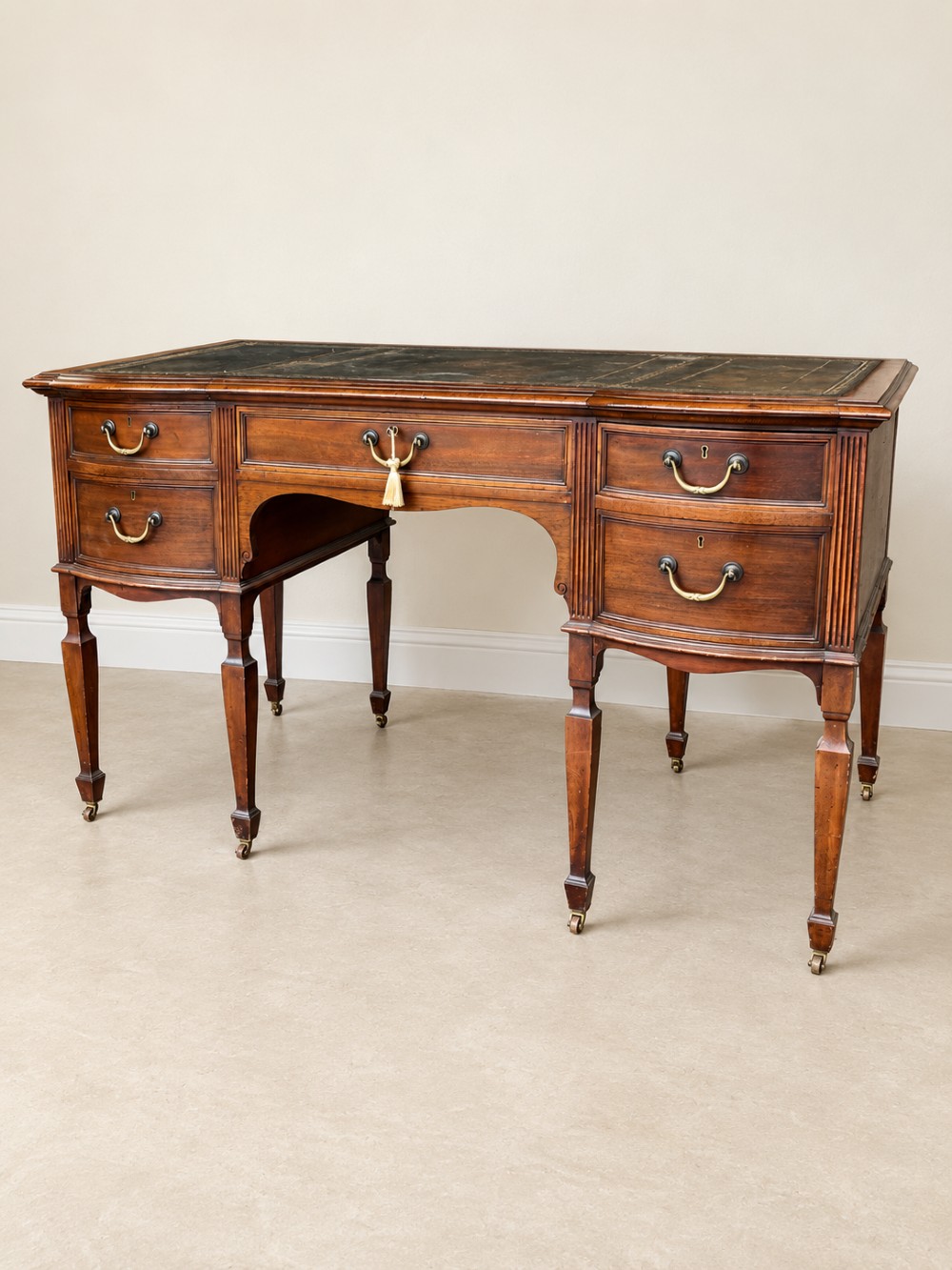 Late nineteenth-century mahogany writing desk featuring an inset dark leather top, five drawers with brass swan-neck handles, fluted pilasters, and tapered legs with brass castors. View III