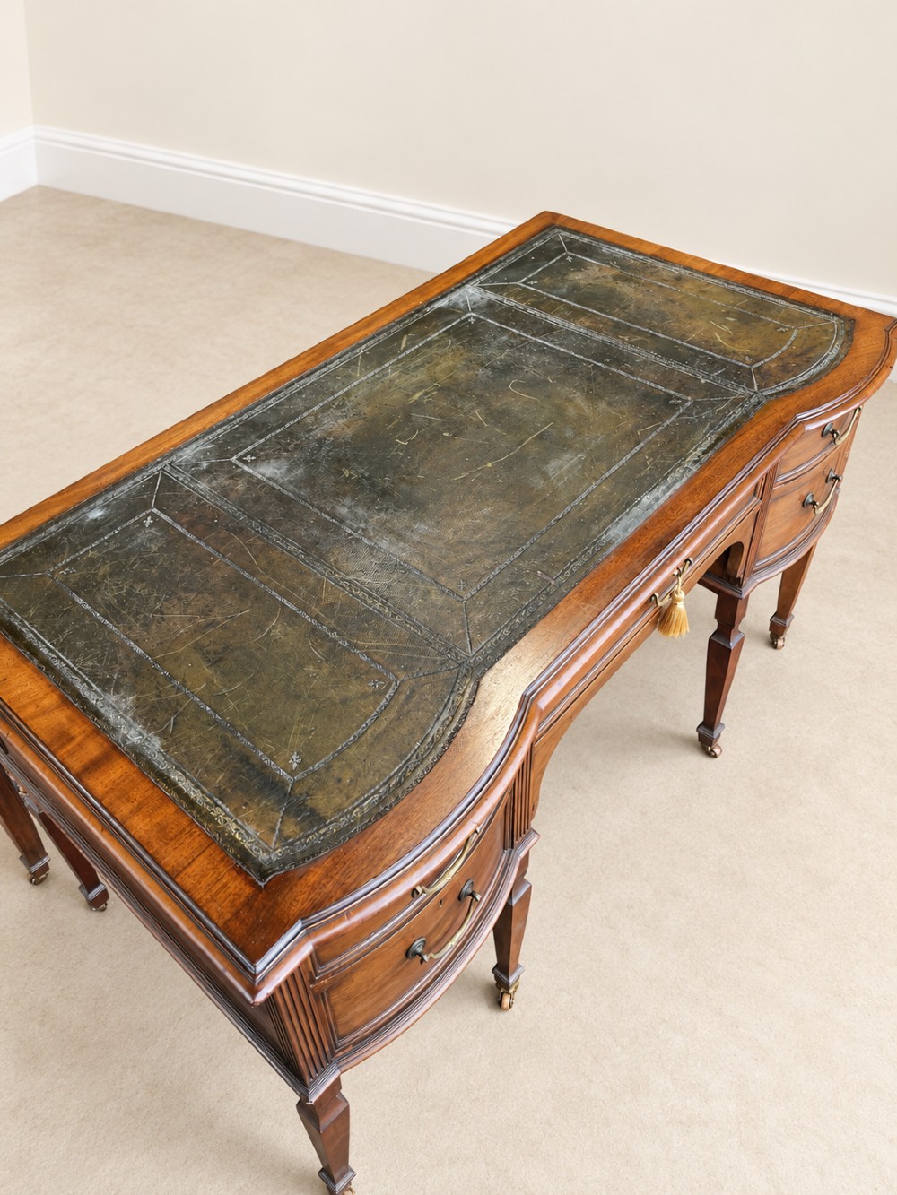Late nineteenth-century mahogany writing desk featuring an inset dark leather top, five drawers with brass swan-neck handles, fluted pilasters, and tapered legs with brass castors. View V
