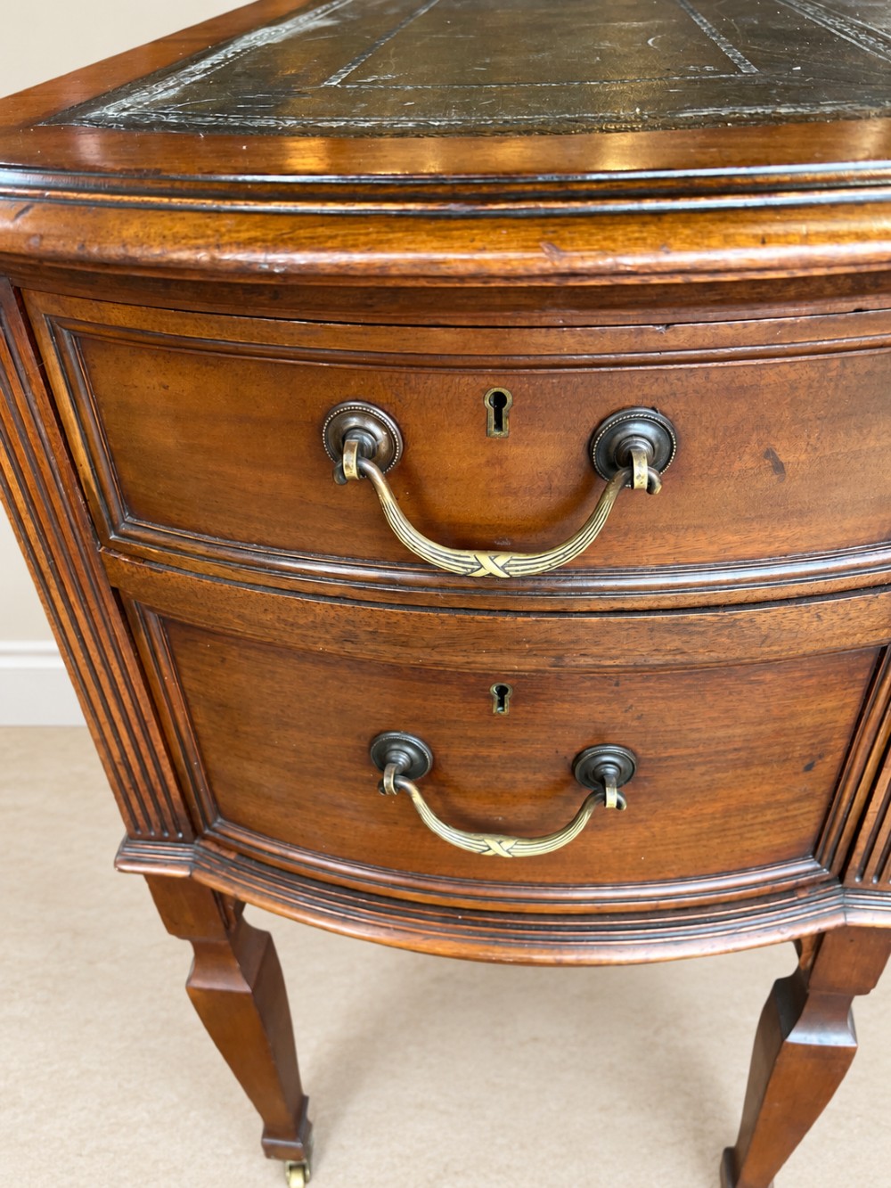 Late nineteenth-century mahogany writing desk featuring an inset dark leather top, five drawers with brass swan-neck handles, fluted pilasters, and tapered legs with brass castors. View VII