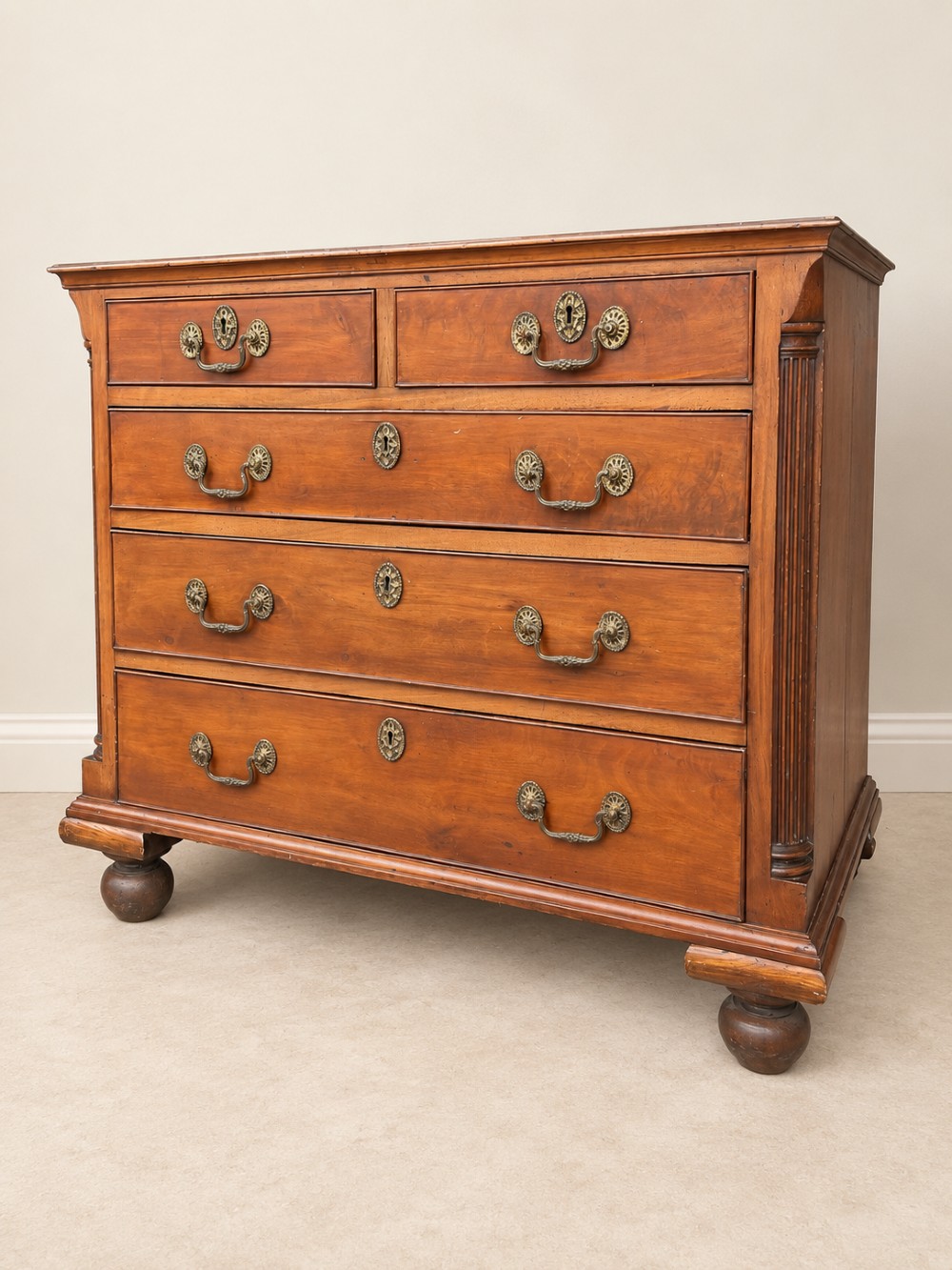 A small Georgian mahogany chest of drawers featuring two short over three long drawers with decorative brass handles, fluted quarter columns, and turned bun feet.