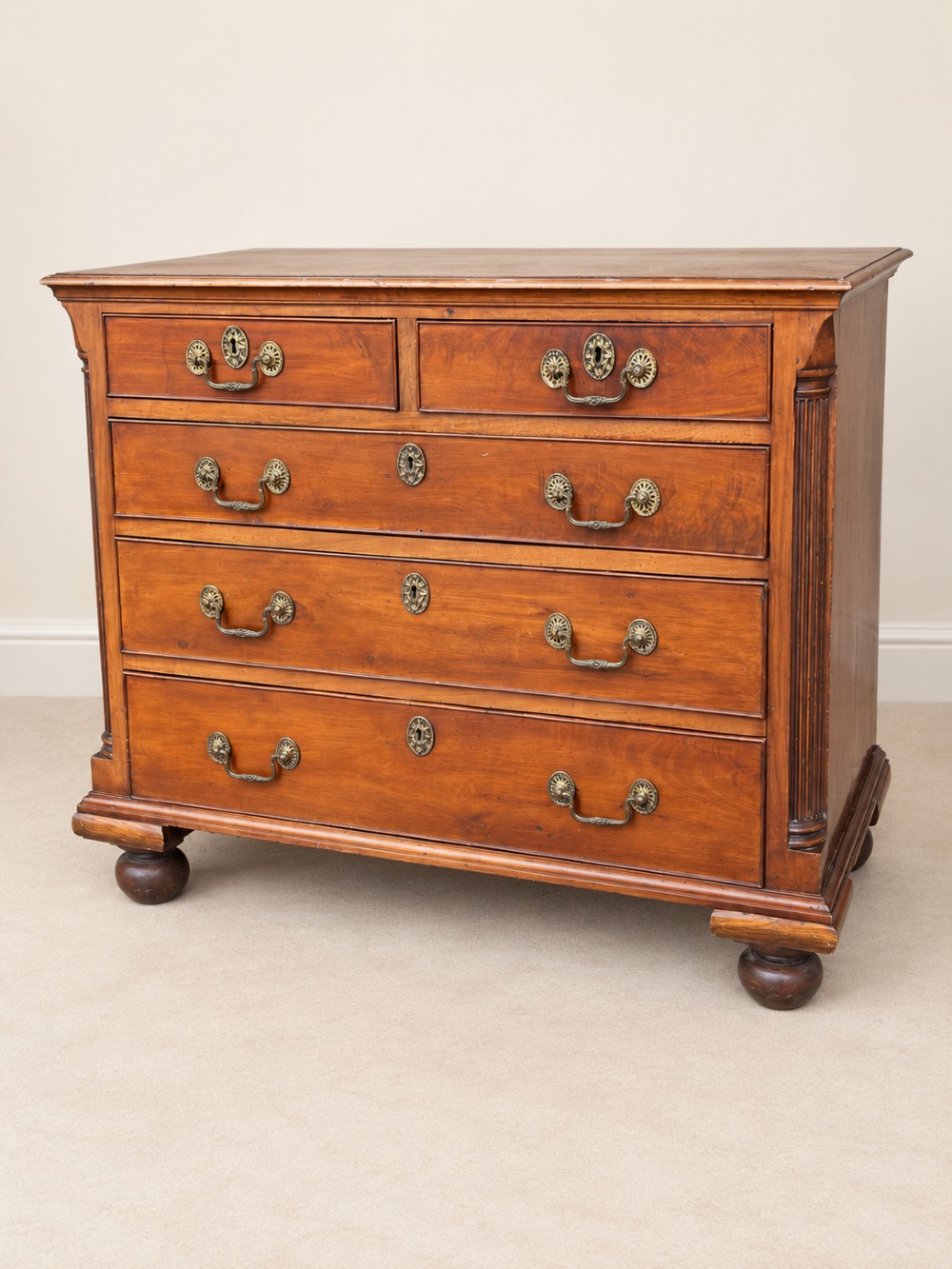 A small Georgian mahogany chest of drawers featuring two short over three long drawers with decorative brass handles, fluted quarter columns, and turned bun feet. View II