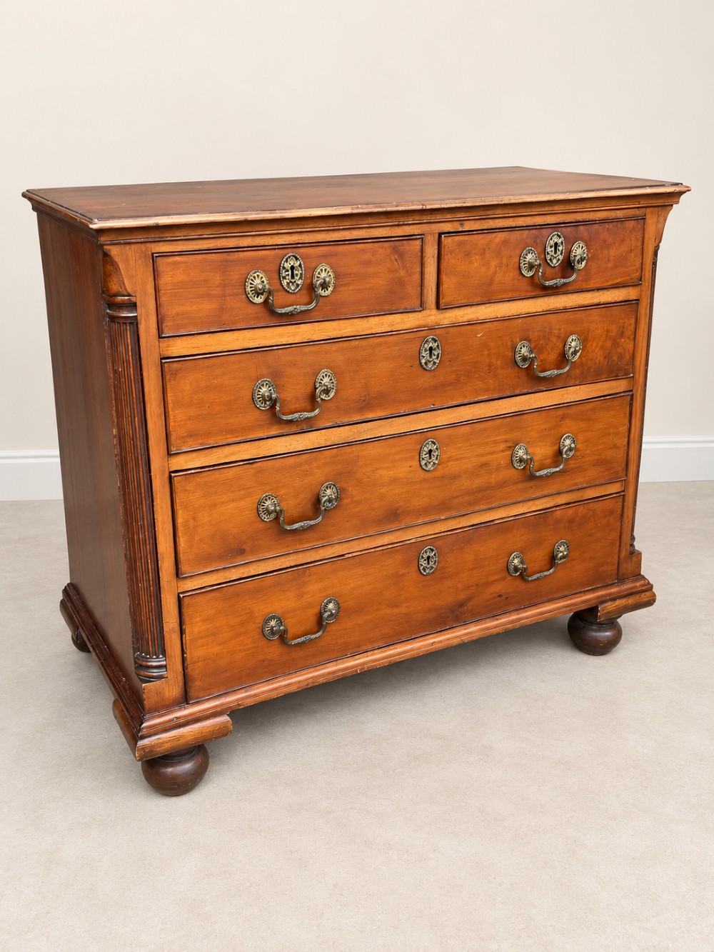 A small Georgian mahogany chest of drawers featuring two short over three long drawers with decorative brass handles, fluted quarter columns, and turned bun feet. View IV