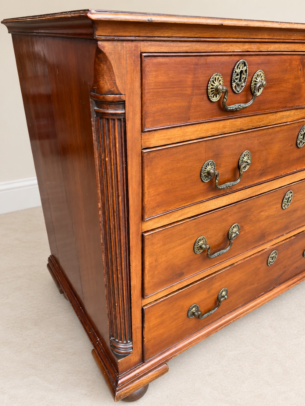 A small Georgian mahogany chest of drawers featuring two short over three long drawers with decorative brass handles, fluted quarter columns, and turned bun feet. View VI