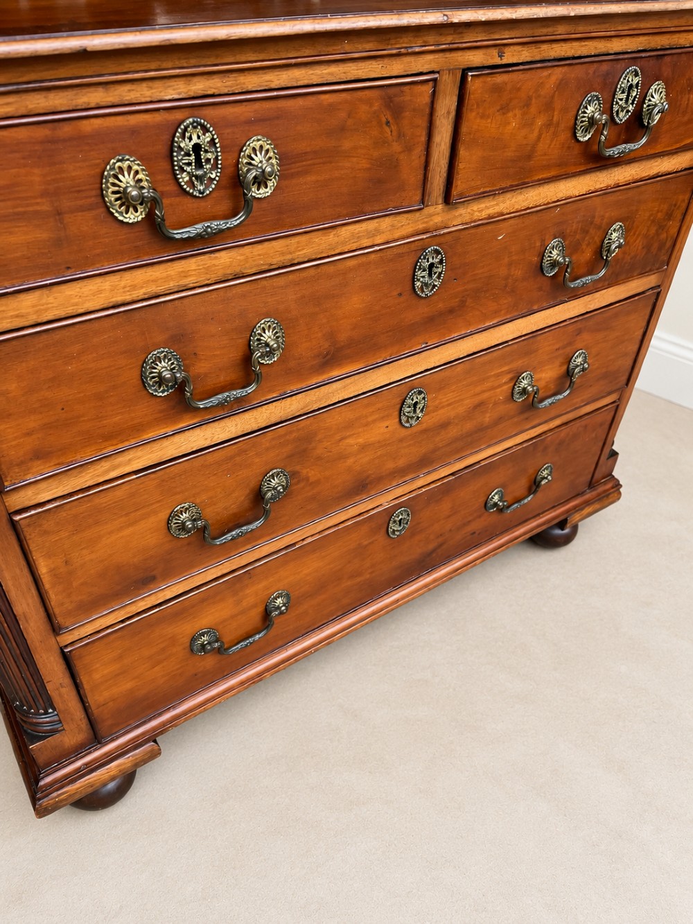 A small Georgian mahogany chest of drawers featuring two short over three long drawers with decorative brass handles, fluted quarter columns, and turned bun feet. View VIII
