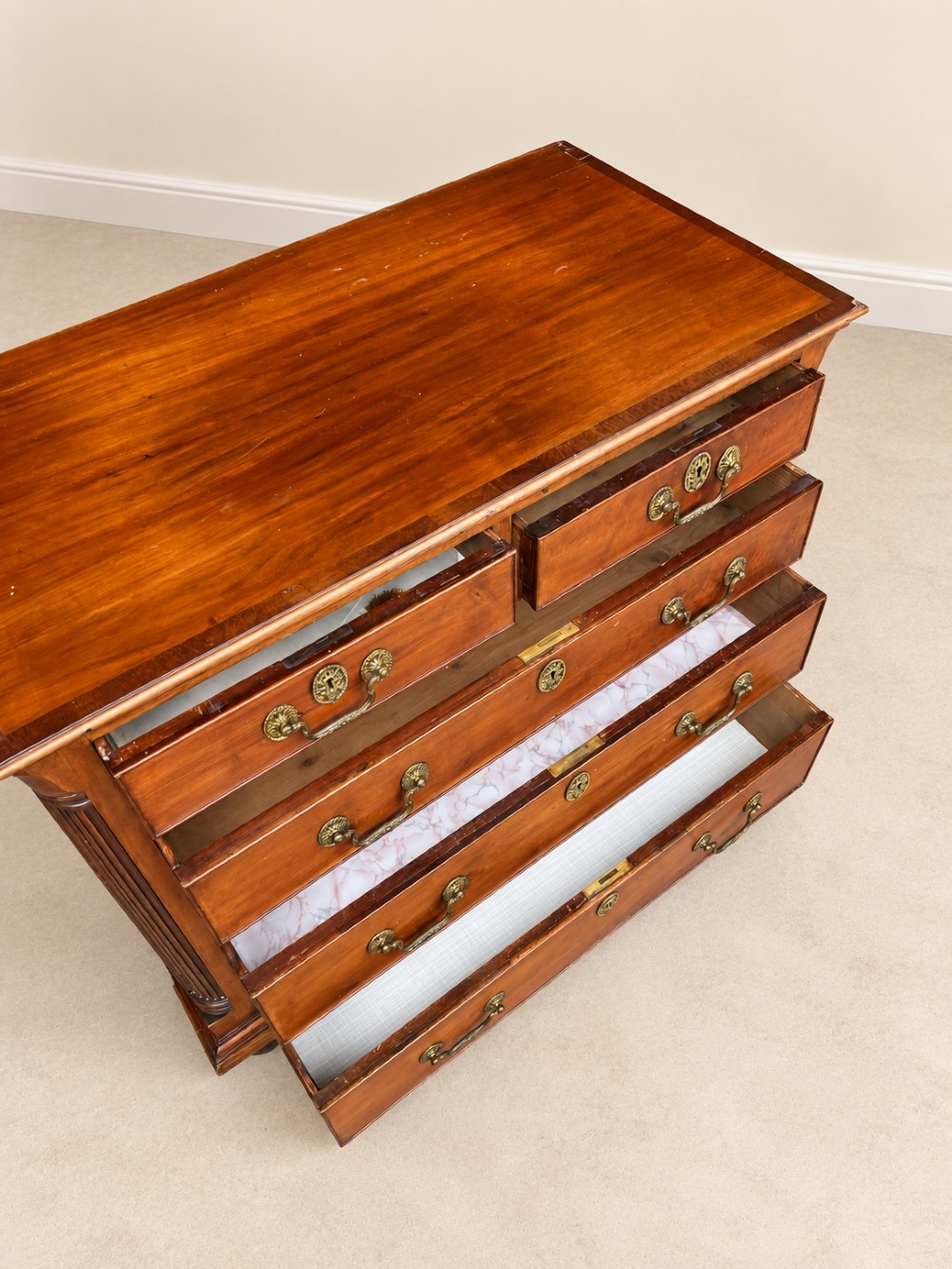 A small Georgian mahogany chest of drawers featuring two short over three long drawers with decorative brass handles, fluted quarter columns, and turned bun feet. View IX