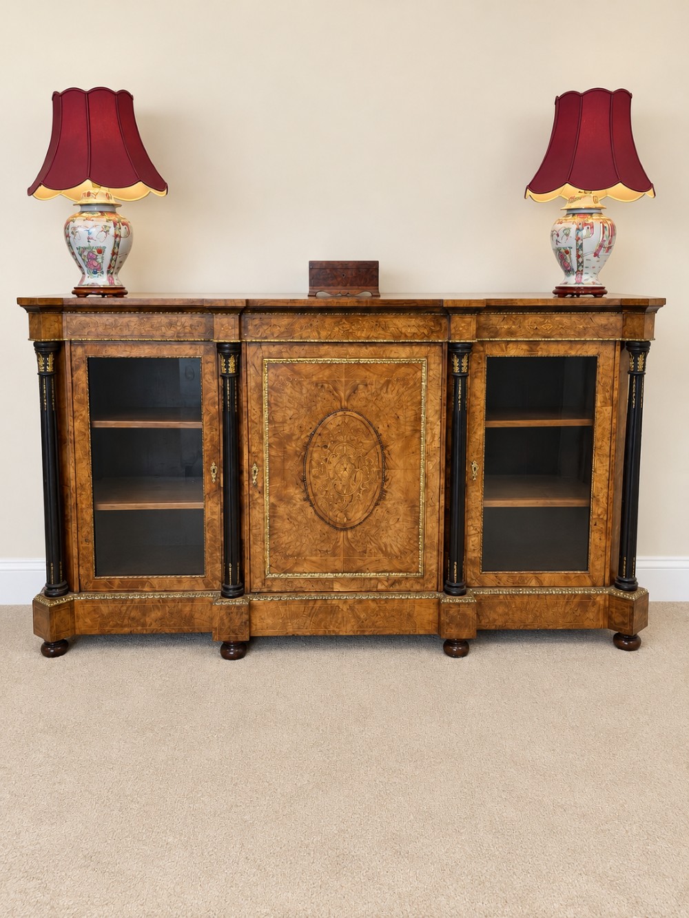 A 19th-century burr walnut credenza with a central marquetry-inlaid door flanked by two glass-front display cabinets and ebonised columns with gilt metal mounts.