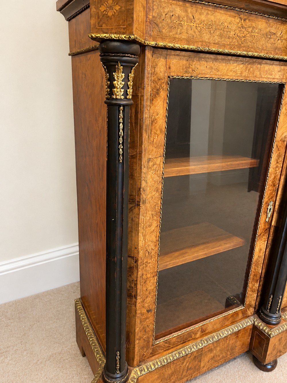 A 19th-century burr walnut credenza with a central marquetry-inlaid door flanked by two glass-front display cabinets and ebonised columns with gilt metal mounts. View VI