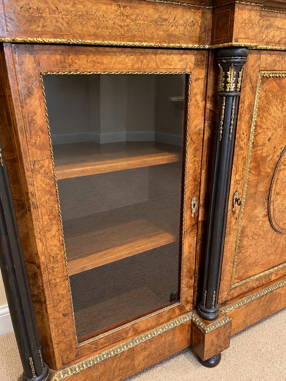 A 19th-century burr walnut credenza with a central marquetry-inlaid door flanked by two glass-front display cabinets and ebonised columns with gilt metal mounts. View VIII