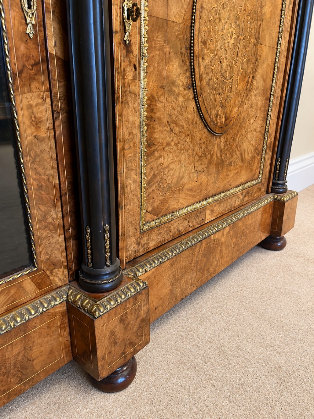 A 19th-century burr walnut credenza with a central marquetry-inlaid door flanked by two glass-front display cabinets and ebonised columns with gilt metal mounts. View IX