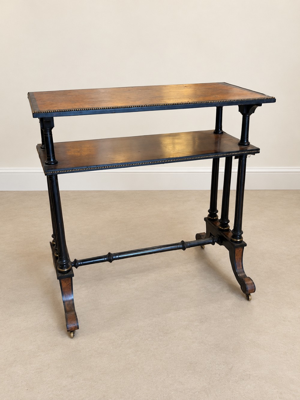 A 19th-century two-tier side table with a burr walnut surface, ebonised turned column legs, brass beaded borders, and scrolled feet on castors. View III