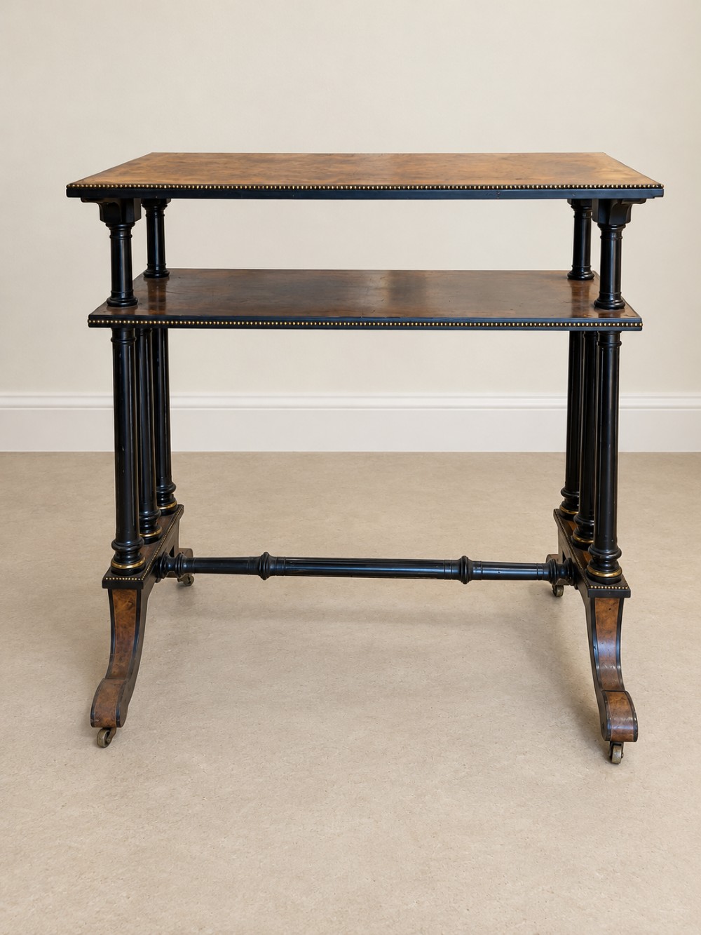 A 19th-century two-tier side table with a burr walnut surface, ebonised turned column legs, brass beaded borders, and scrolled feet on castors. View IV