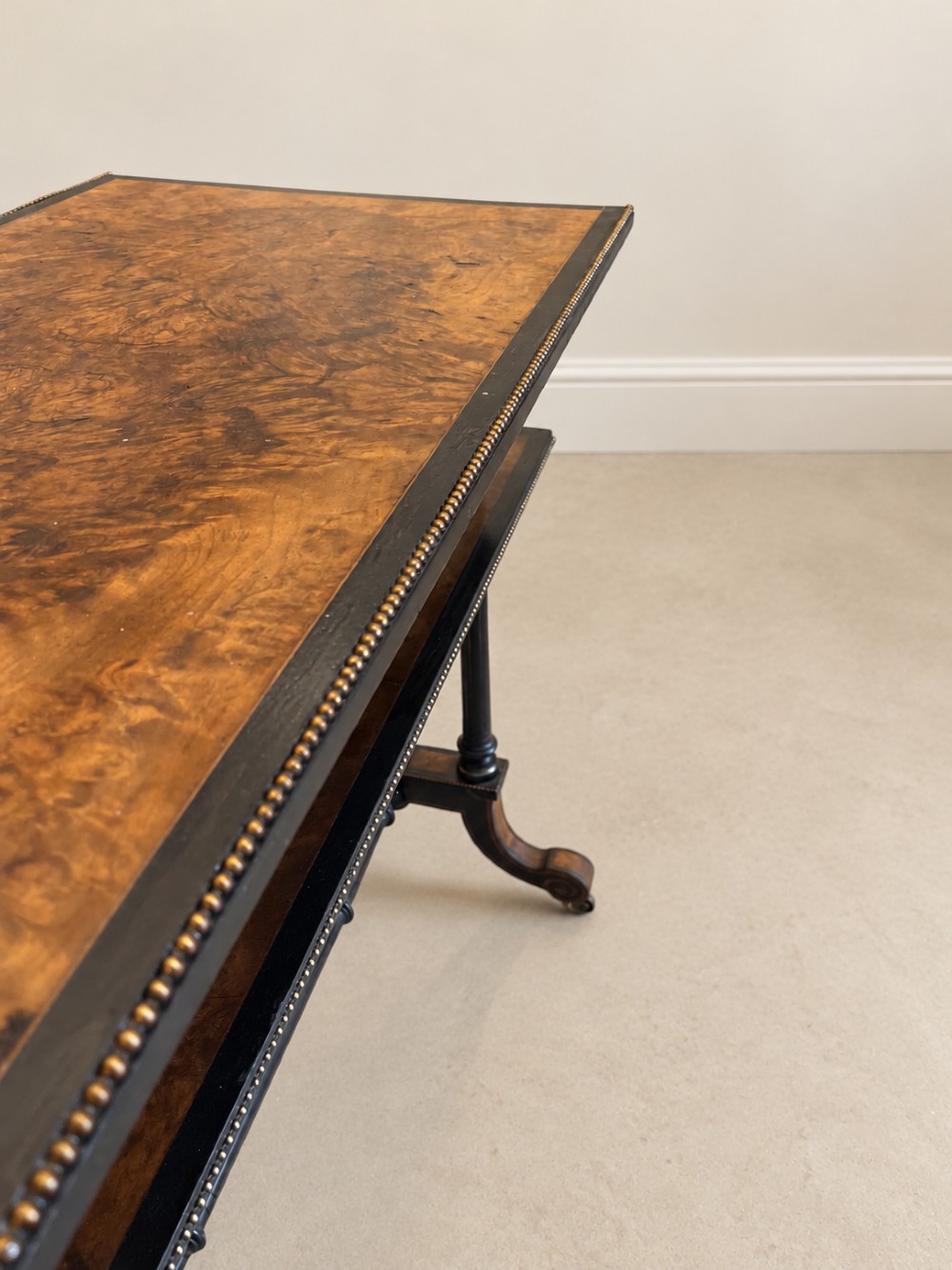 A 19th-century two-tier side table with a burr walnut surface, ebonised turned column legs, brass beaded borders, and scrolled feet on castors. View VII