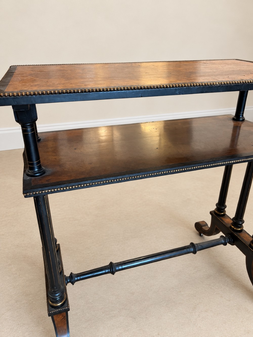 A 19th-century two-tier side table with a burr walnut surface, ebonised turned column legs, brass beaded borders, and scrolled feet on castors. View IX