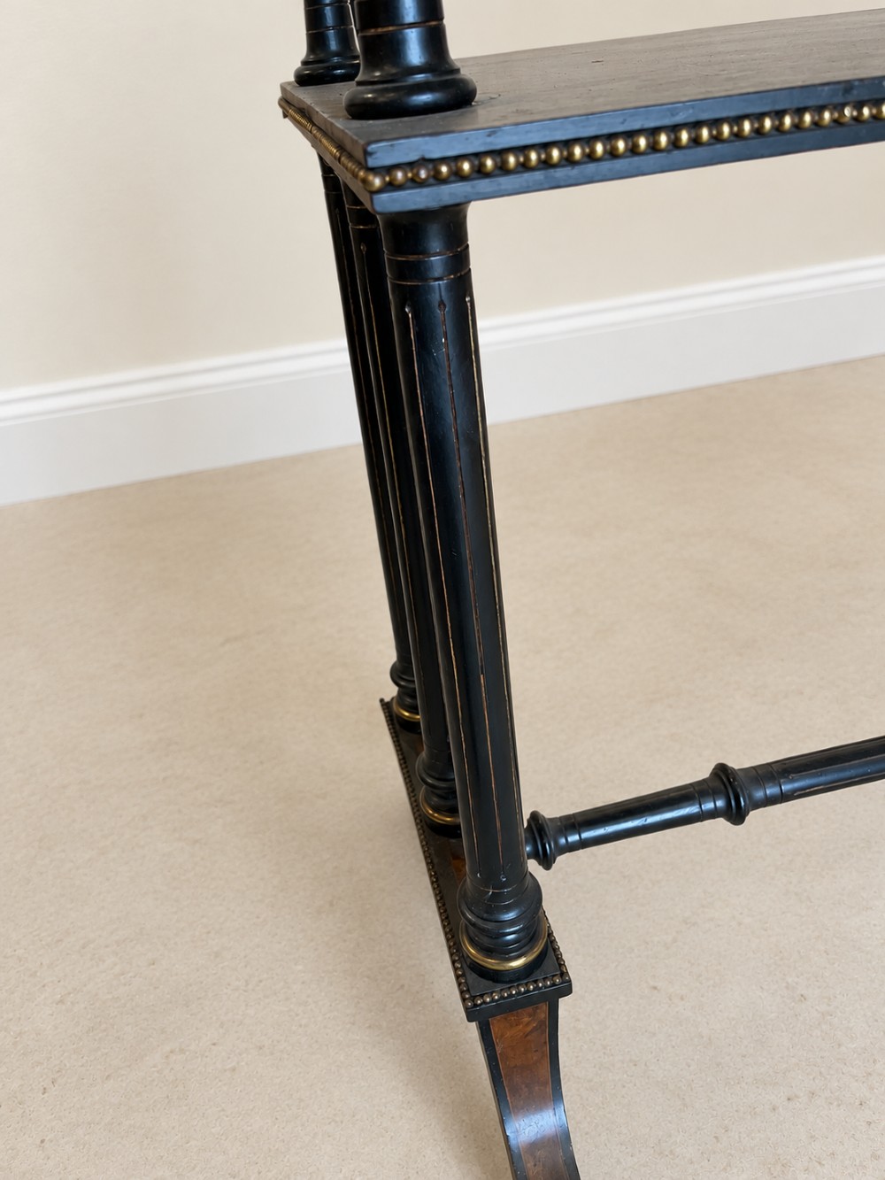 A 19th-century two-tier side table with a burr walnut surface, ebonised turned column legs, brass beaded borders, and scrolled feet on castors. View X