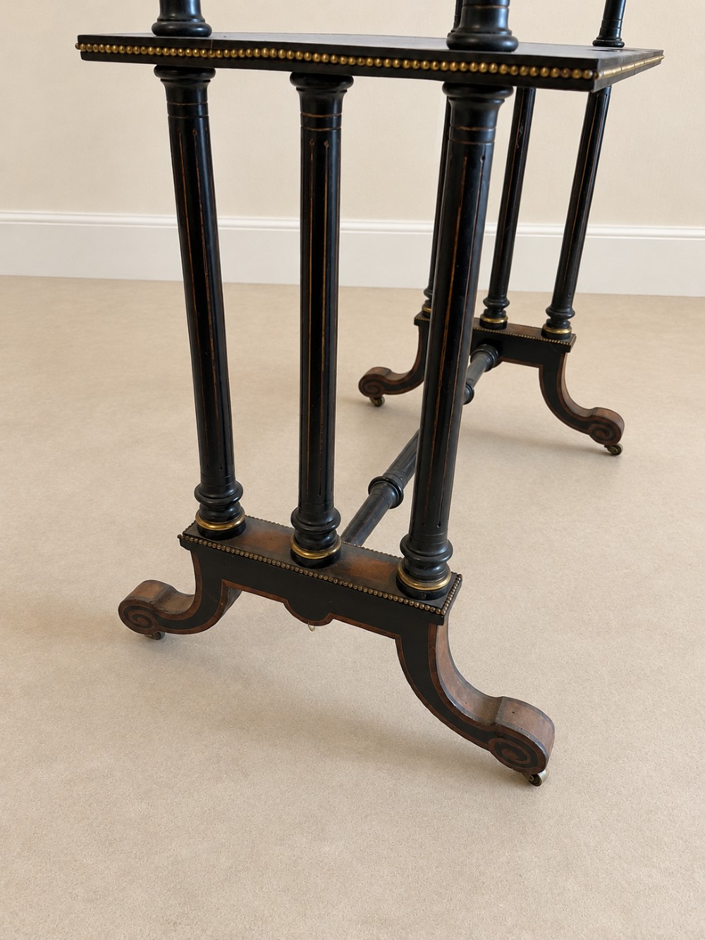 A 19th-century two-tier side table with a burr walnut surface, ebonised turned column legs, brass beaded borders, and scrolled feet on castors. View XI