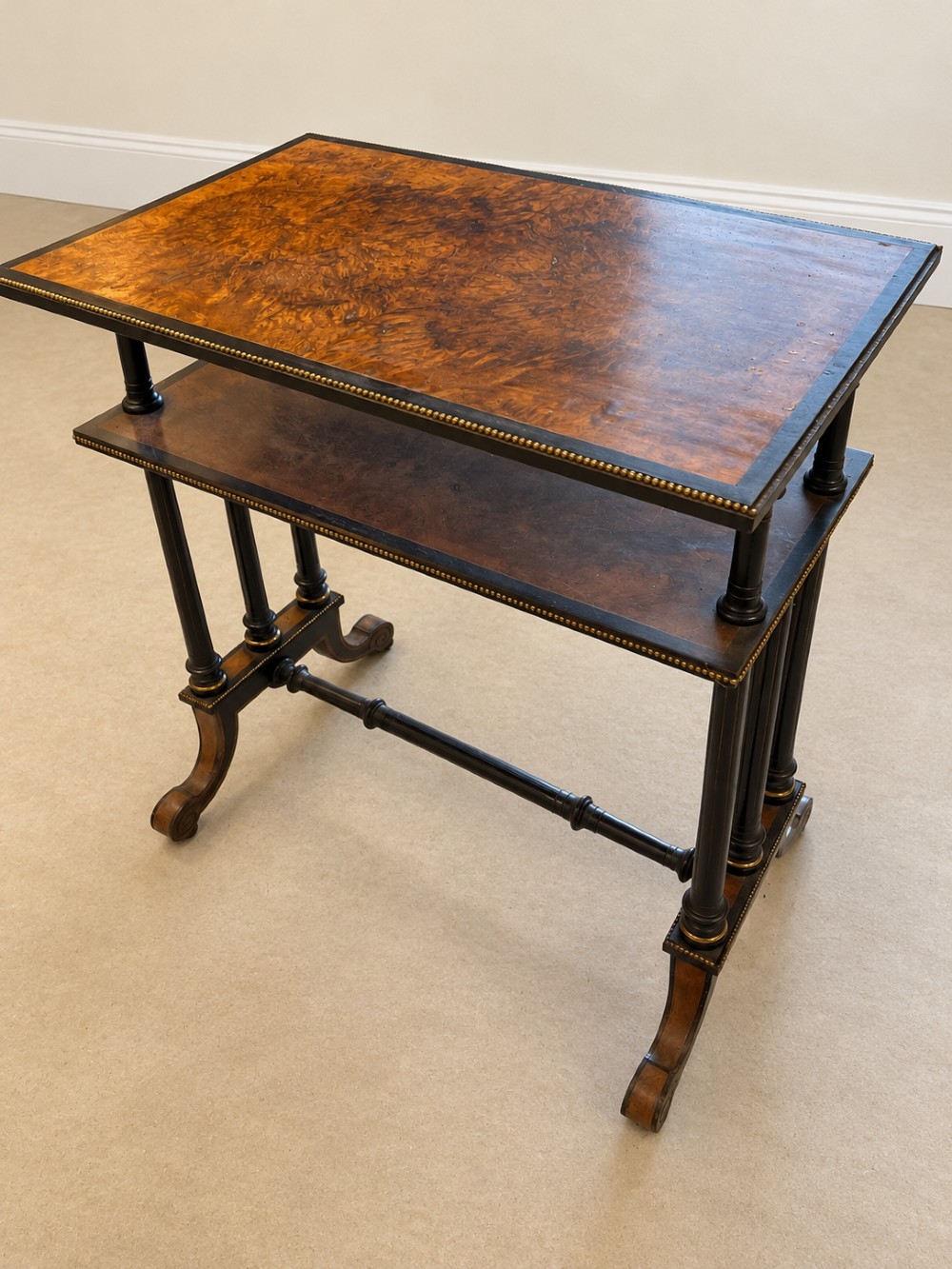A 19th-century two-tier side table with a burr walnut surface, ebonised turned column legs, brass beaded borders, and scrolled feet on castors. View XII