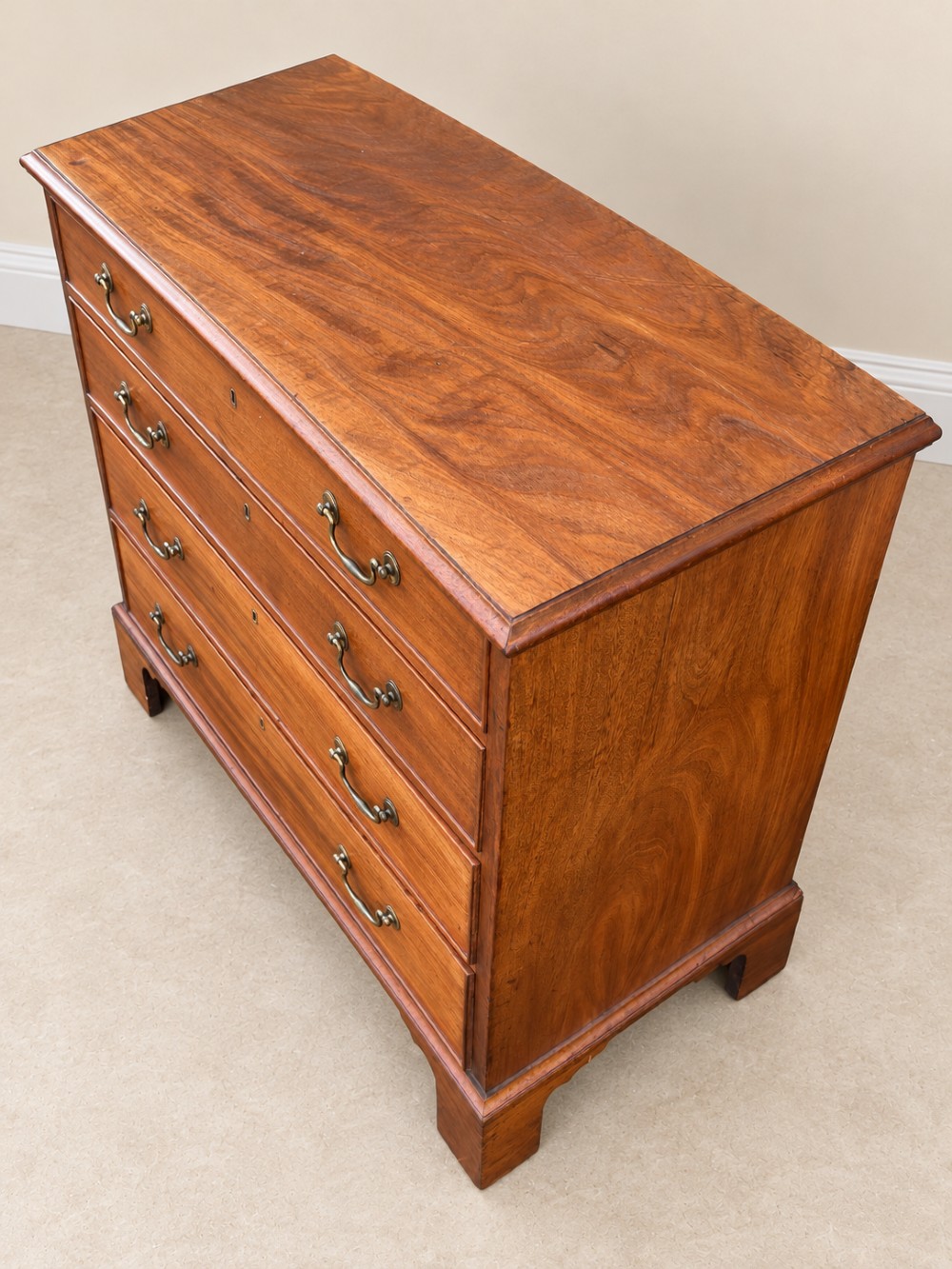 An antique Georgian mahogany chest of drawers featuring four graduated drawers with brass swan-neck handles, keyhole escutcheons, and bracket feet. View II