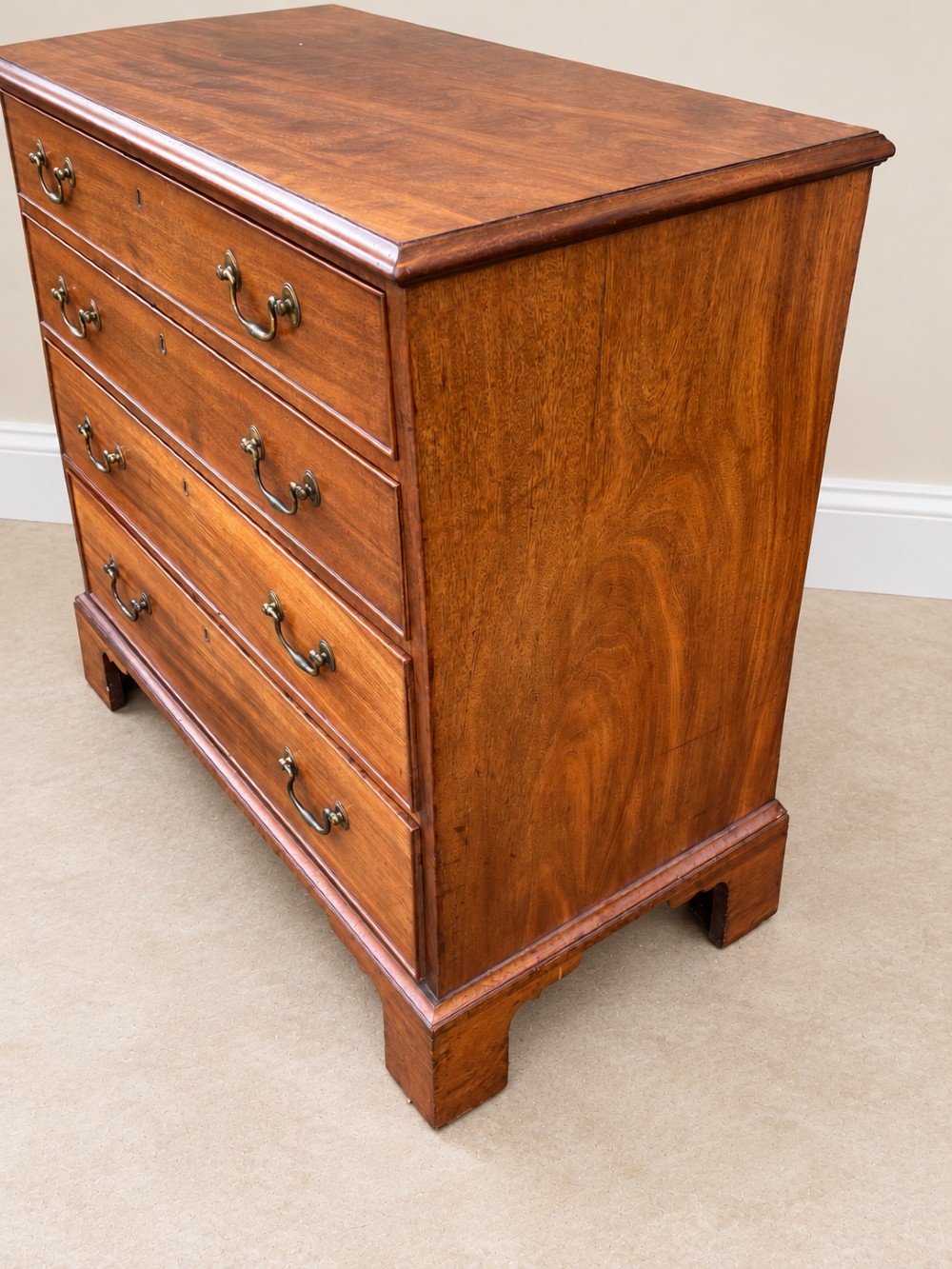 An antique Georgian mahogany chest of drawers featuring four graduated drawers with brass swan-neck handles, keyhole escutcheons, and bracket feet. View III