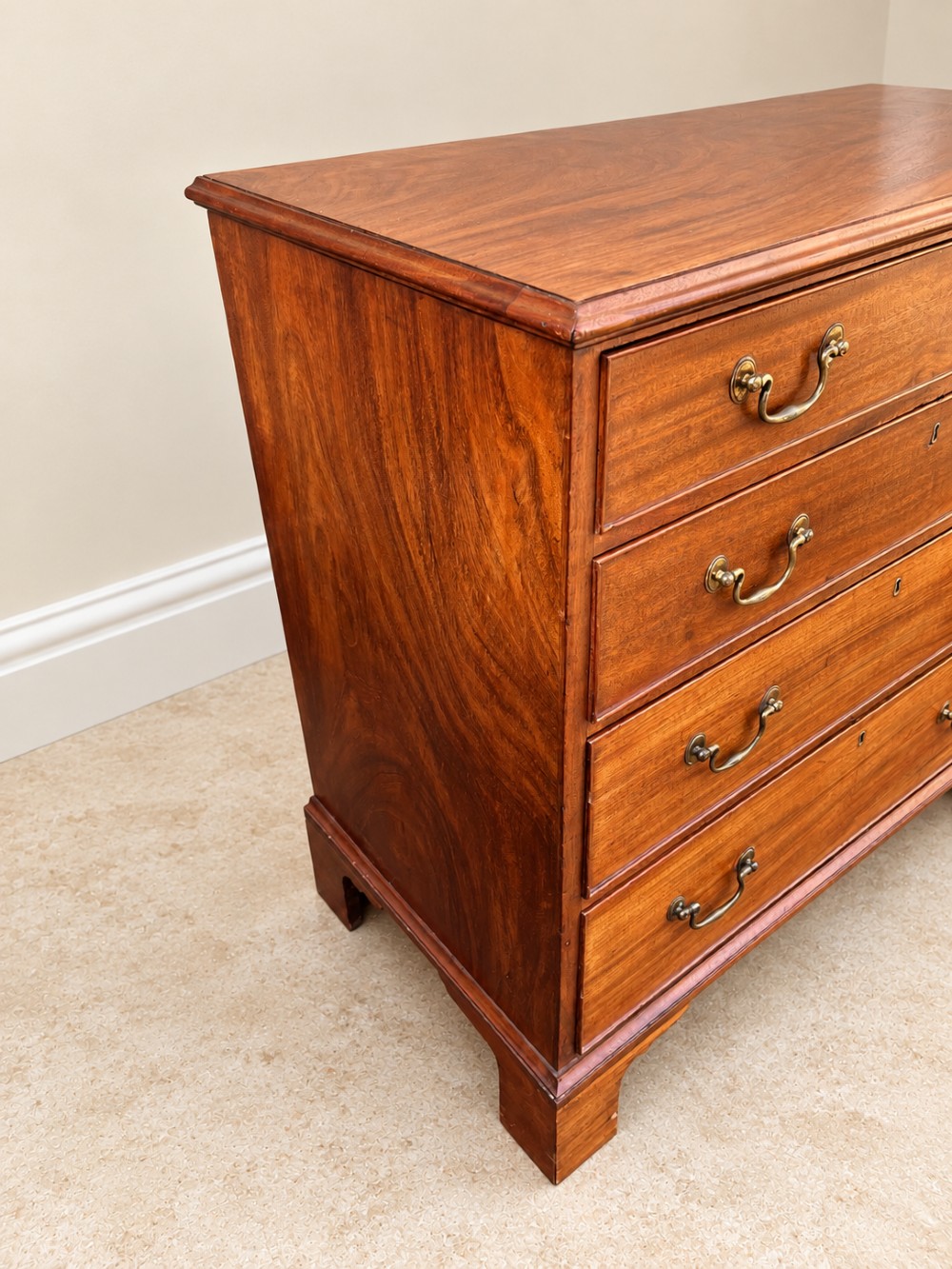 An antique Georgian mahogany chest of drawers featuring four graduated drawers with brass swan-neck handles, keyhole escutcheons, and bracket feet. View V